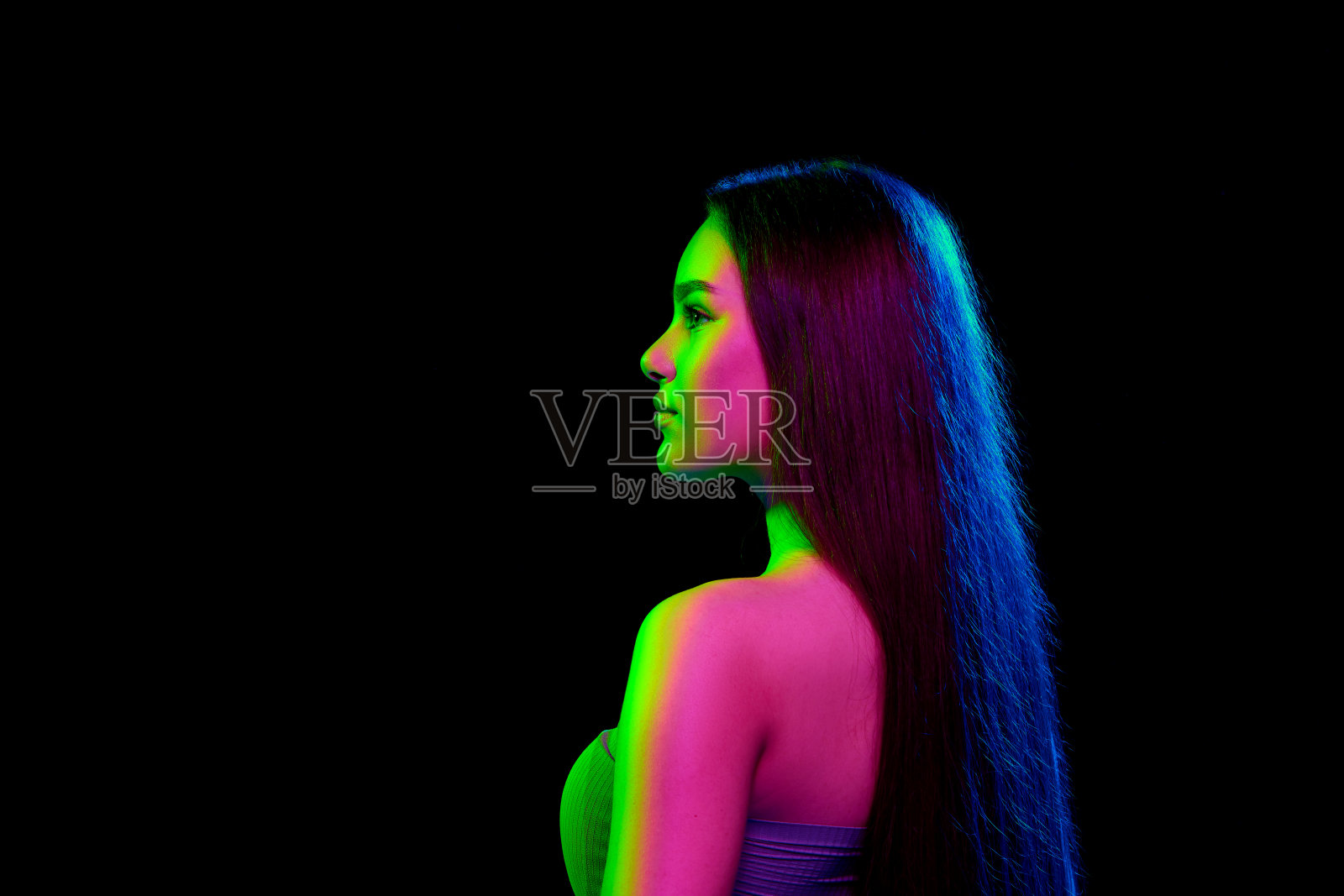 在霓虹灯下，美丽的年轻女孩的侧视图肖像，长而整齐，闪亮的头发在黑色工作室背景下摆姿势照片摄影图片