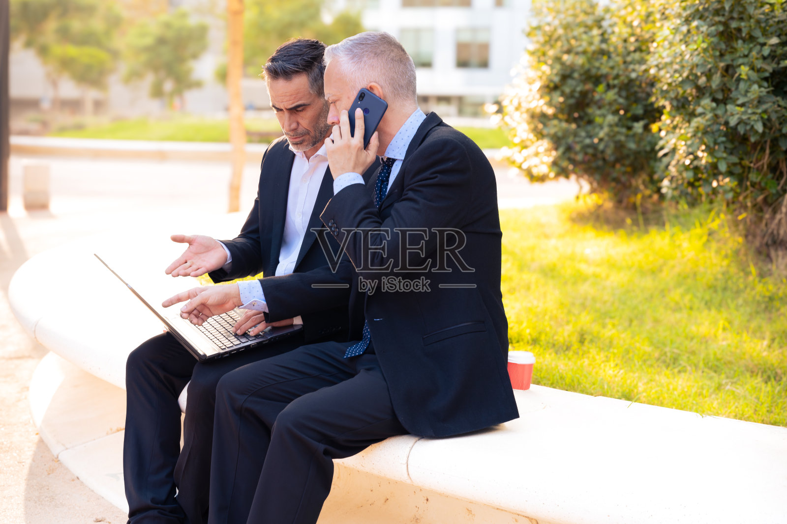 两个商人手里拿着笔记本电脑，看着项目成果。照片摄影图片