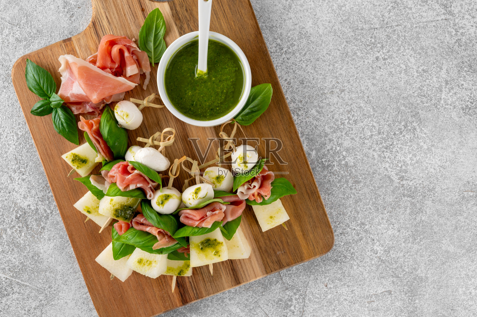 开胃菜，甜瓜，马苏里拉奶酪，火腿和新鲜罗勒，香蒜沙司在石头背景。手指食物。夏季沙拉。照片摄影图片