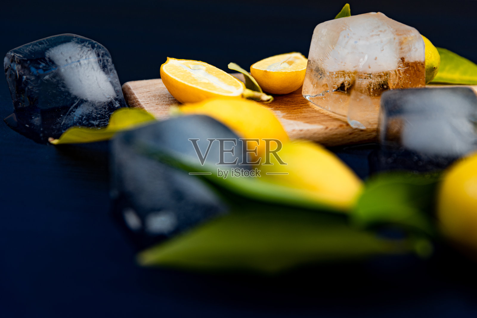 新鲜柠檬与叶子和冰块在深蓝色木制背景照片摄影图片