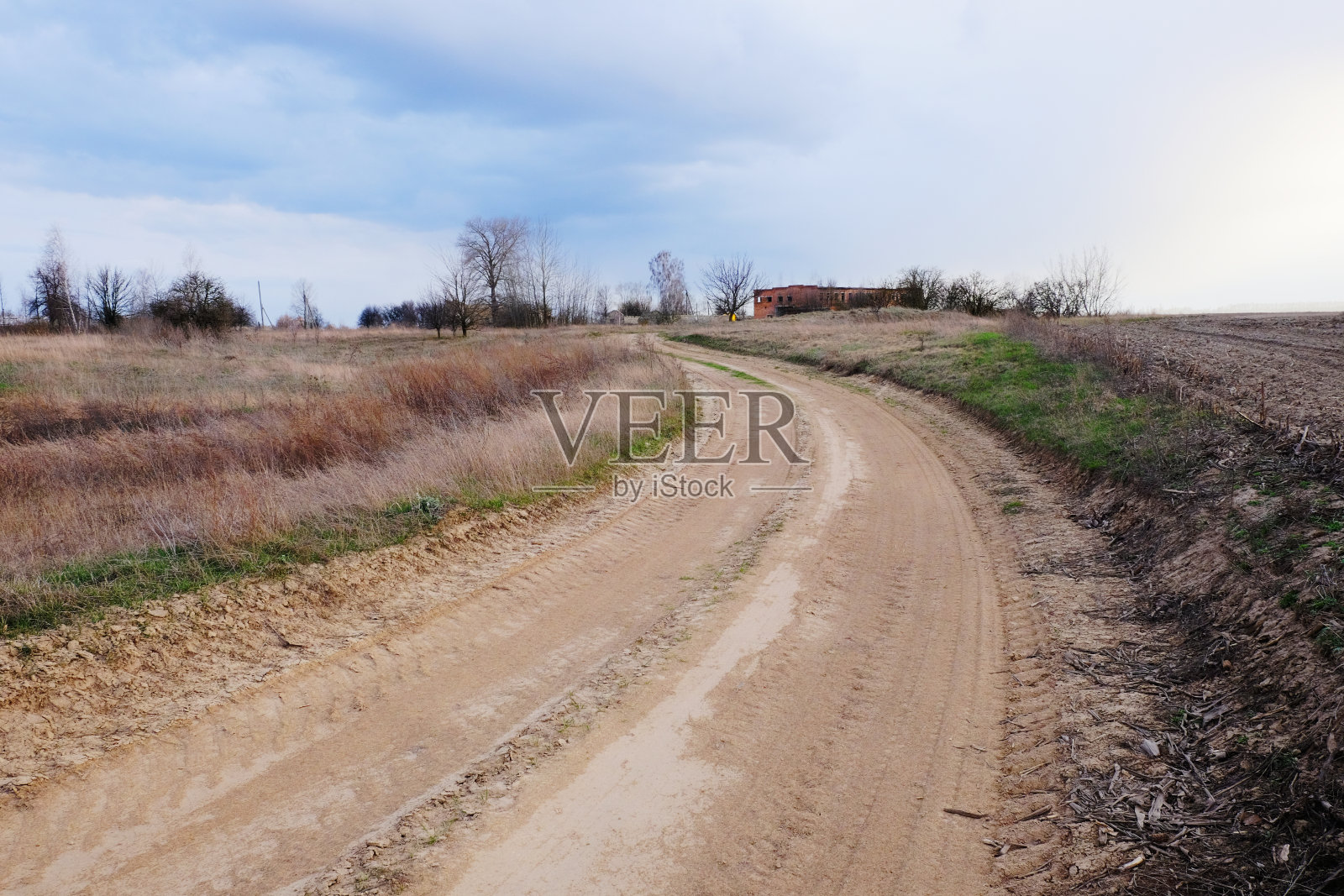 多云的天空下，一条通往一所房子的土路。照片摄影图片