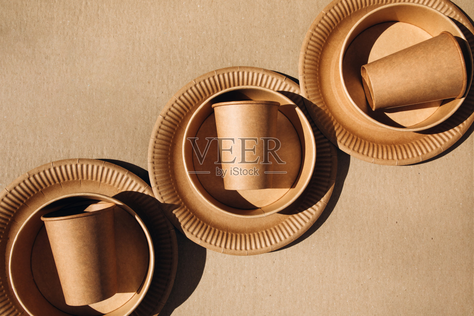 一套纸器皿、杯子和盘子，以棕色为背景。环保，零浪费理念照片摄影图片