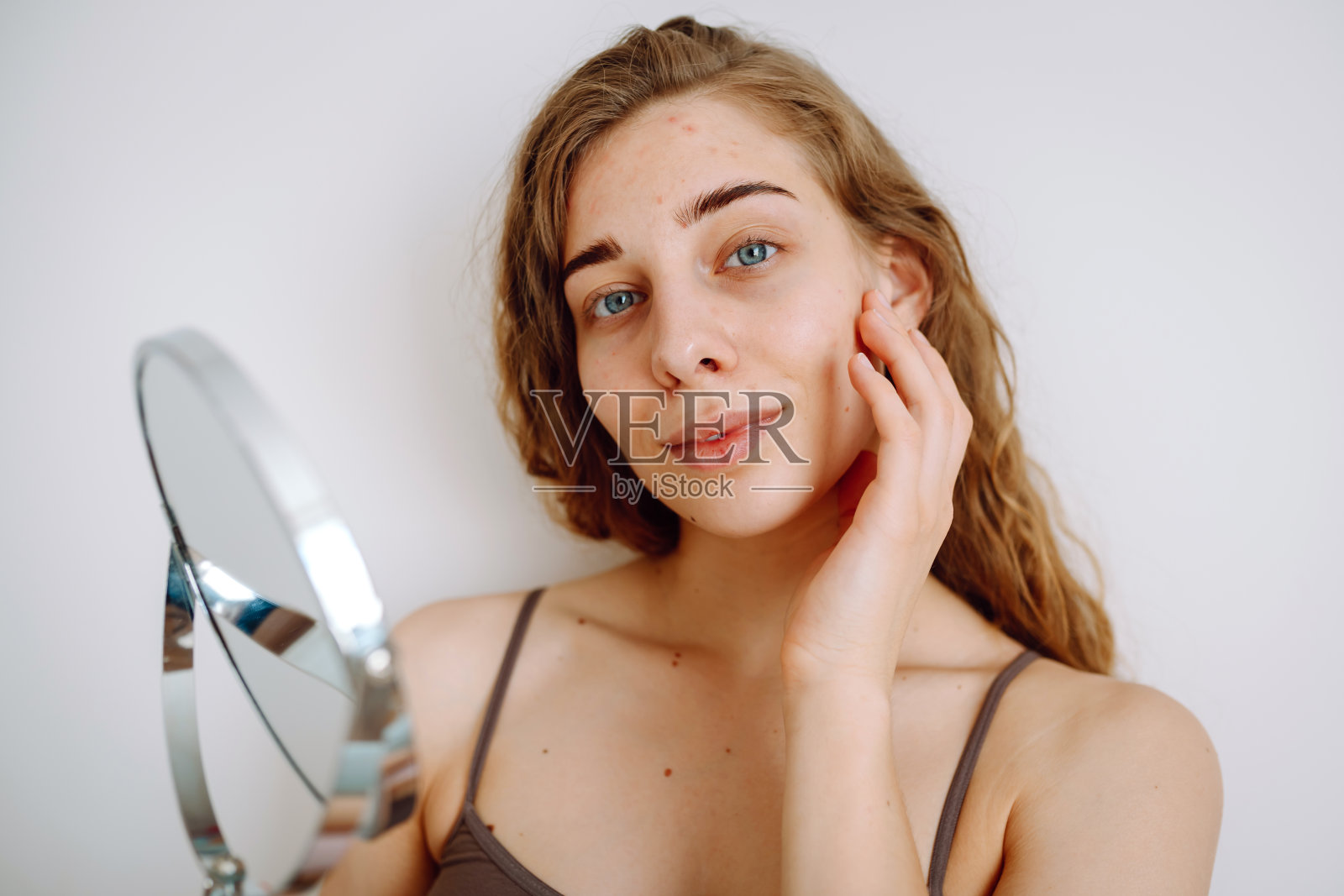 一个漂亮的女人看着镜子，用手摸着自己的脸，检查痤疮和色素沉着。照片摄影图片