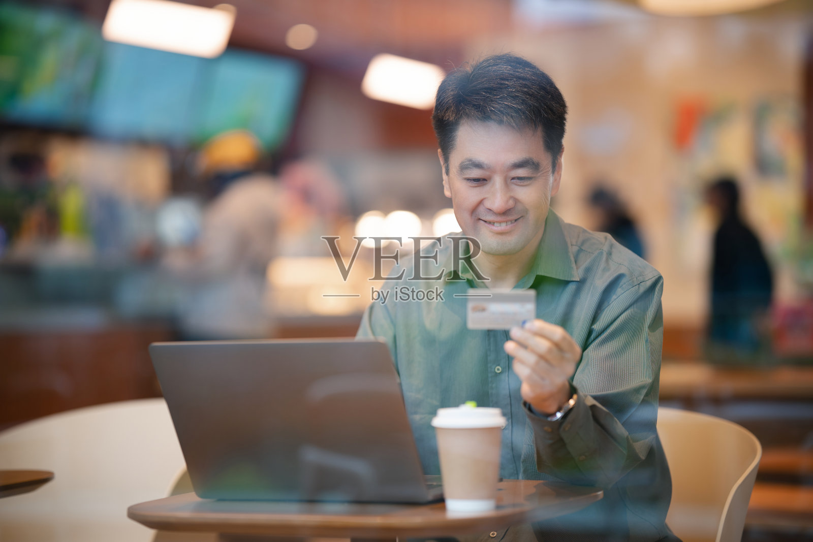 中年成熟男子坐在咖啡店里，用笔记本电脑和信用卡付款照片摄影图片