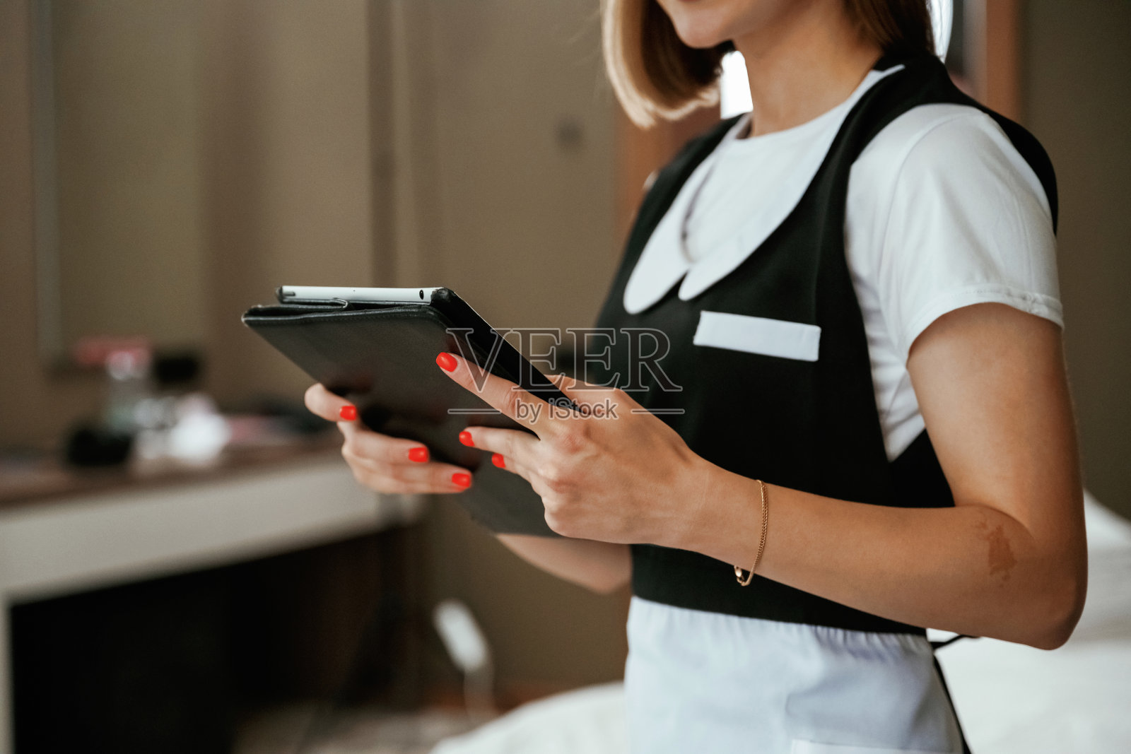 手里拿着黑色的数码平板电脑。年轻的女服务员在旅馆房间里照片摄影图片
