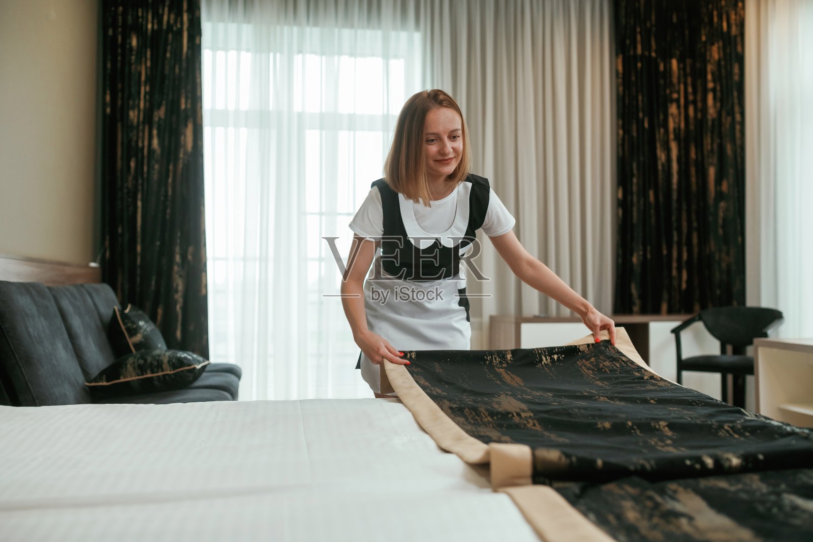 照顾好床铺。年轻的女服务员在旅馆房间里照片摄影图片