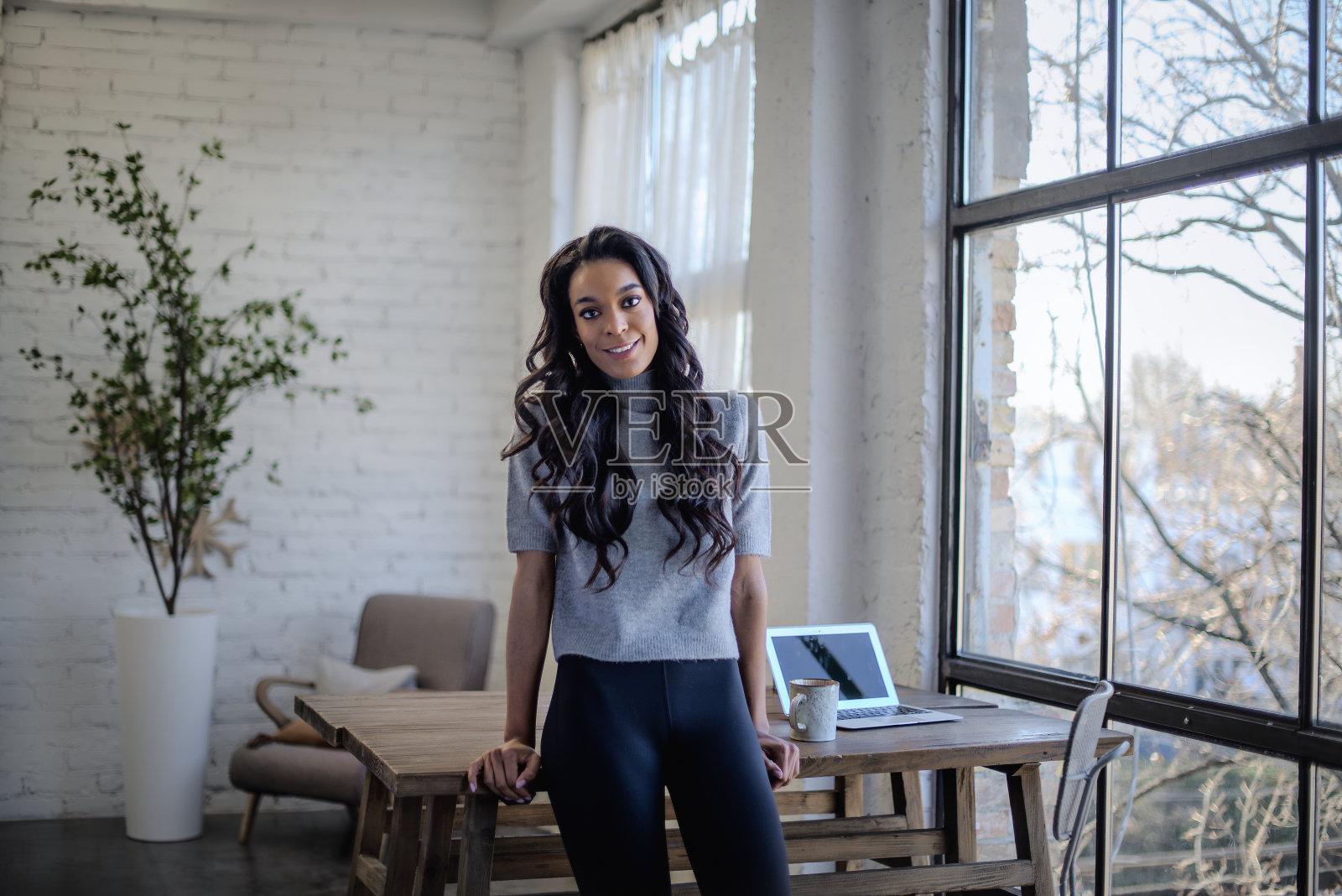 一位非洲裔美国妇女站在靠窗的桌子旁，对着镜头微笑照片摄影图片