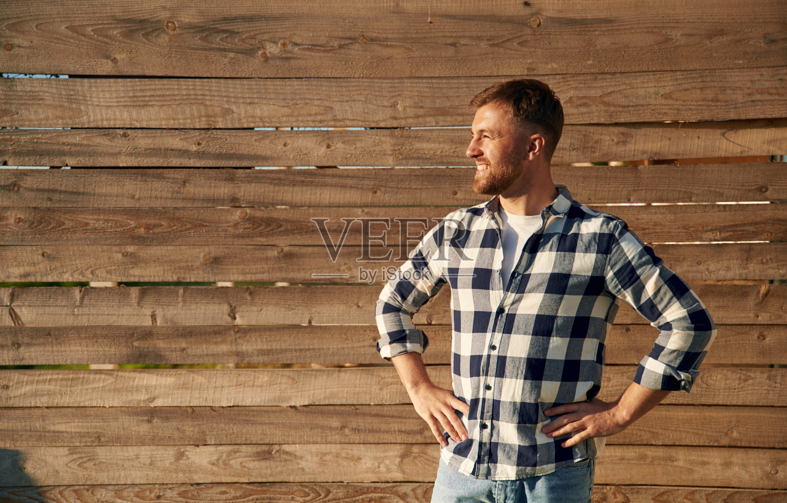 一个穿格子衬衫的人靠着木墙站着照片摄影图片