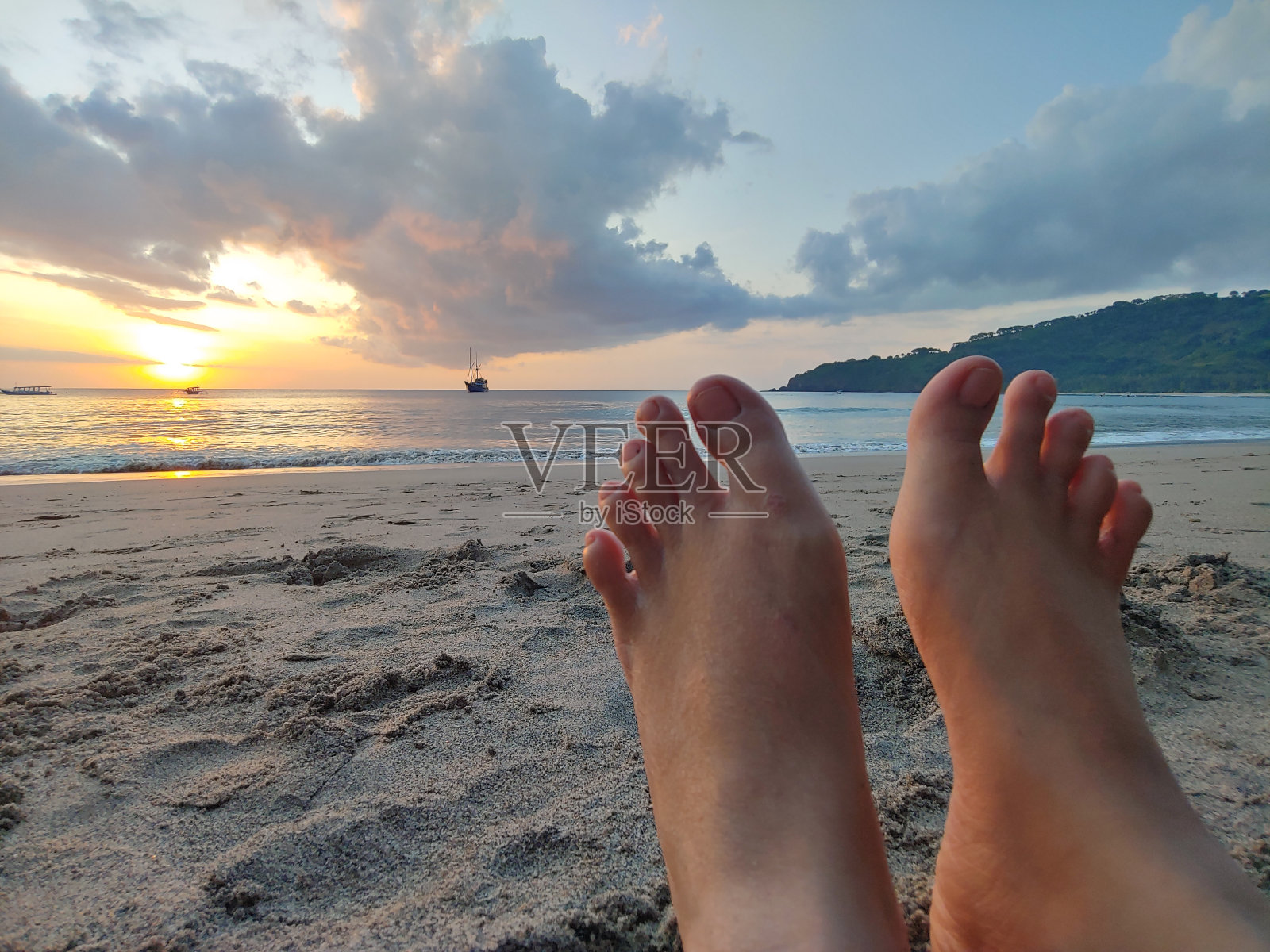 日落时沙滩上女人的腿。照片摄影图片