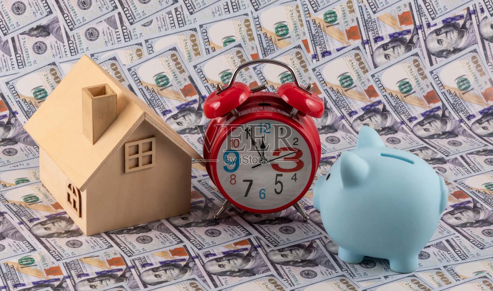 100美元纸币的背景是储蓄罐、象征性的房子和红色闹钟照片摄影图片
