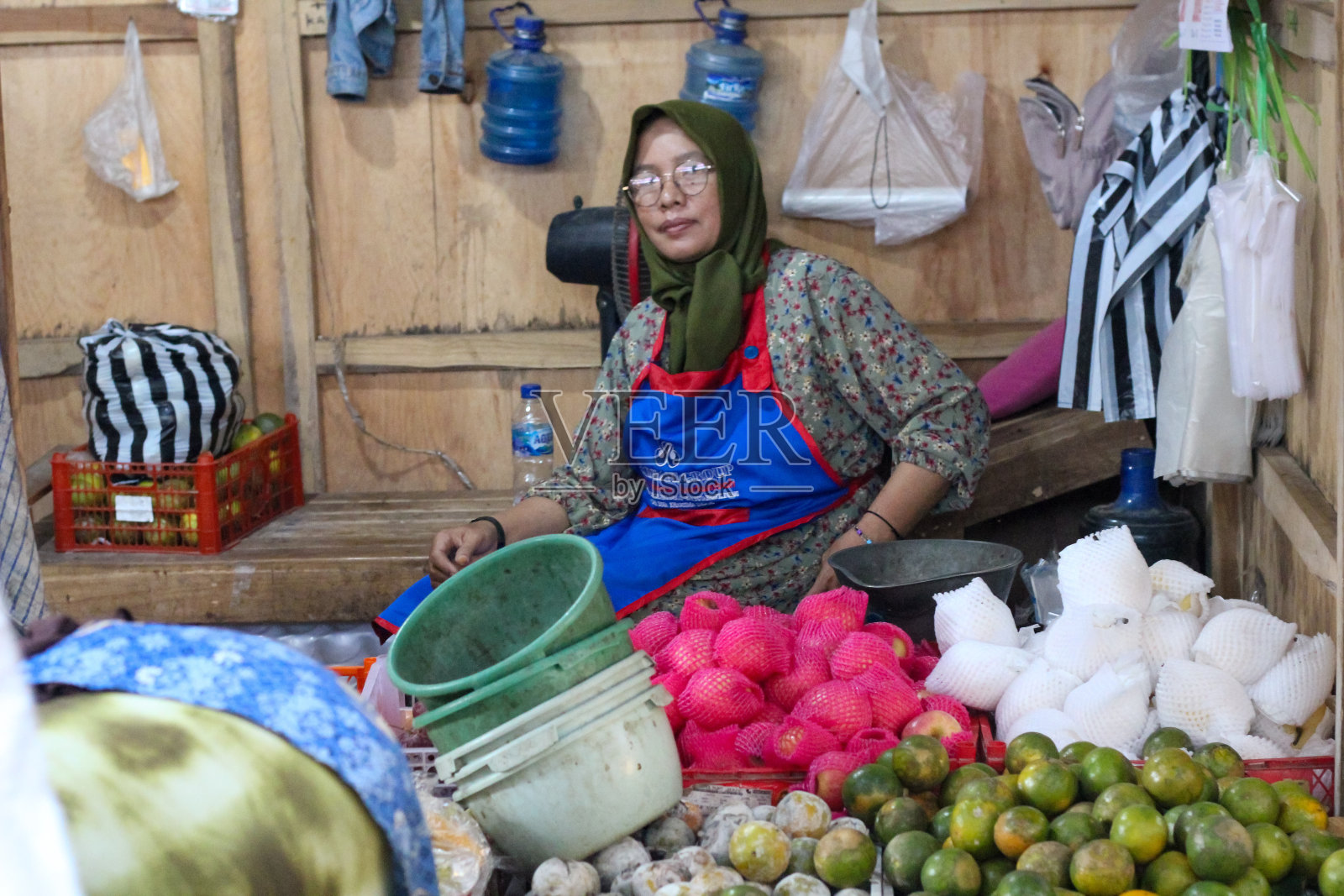 戴着头巾和眼镜的妇女坐在她的市场摊位上出售各种水果照片摄影图片