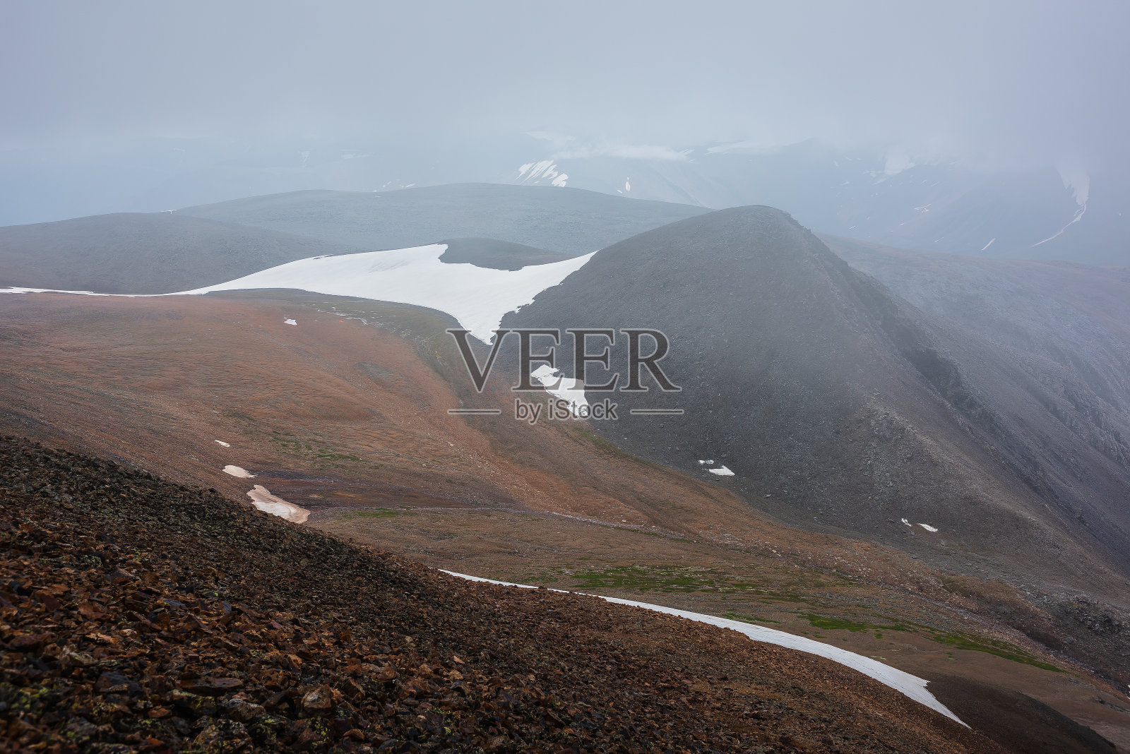 在阴雨的坏天气里，丘陵和山脉的黑暗剪影与厚厚的雾中的雪。宽阔的冰川在多石的山坡和山脉的轮廓在浓雾在灰色的天空。阴冷的景色。照片摄影图片