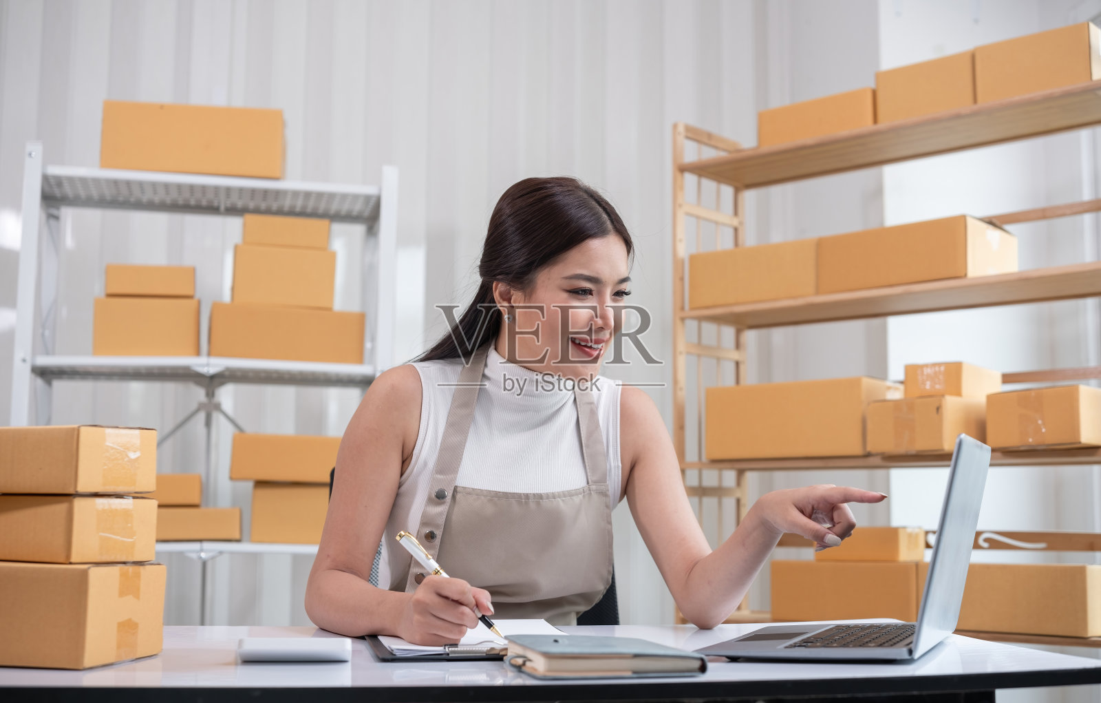 在一个有架子和笔记本电脑的现代工作空间里，女人正在为网上销售的商品装箱照片摄影图片