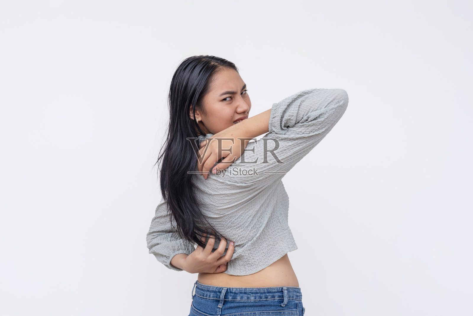 一个恼火的亚洲女人挣扎着去摸她背上的痒，表现出片刻的不适。孤立在白色背景上。照片摄影图片