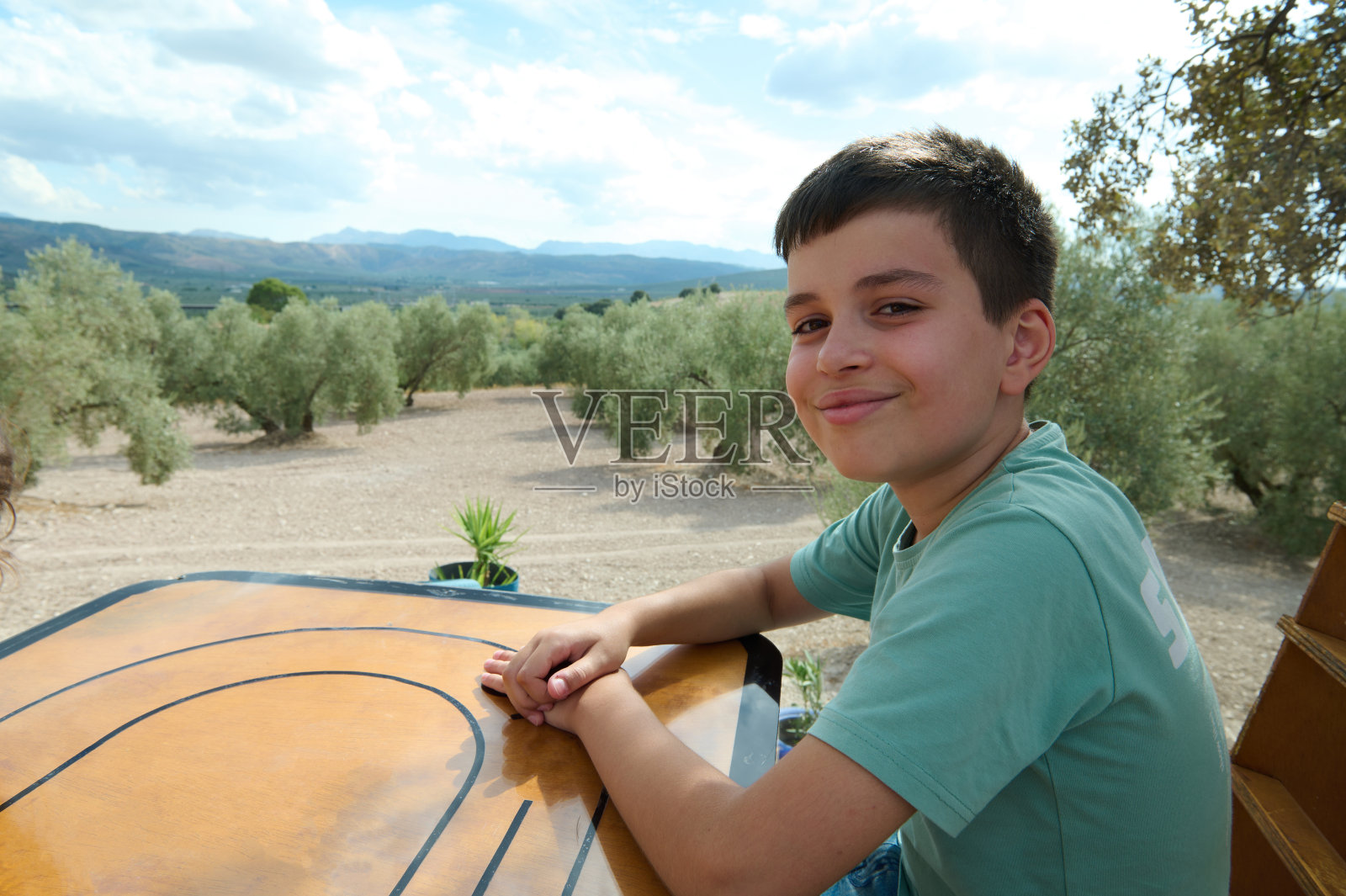 微笑的男孩坐在户外，身后是橄榄树照片摄影图片