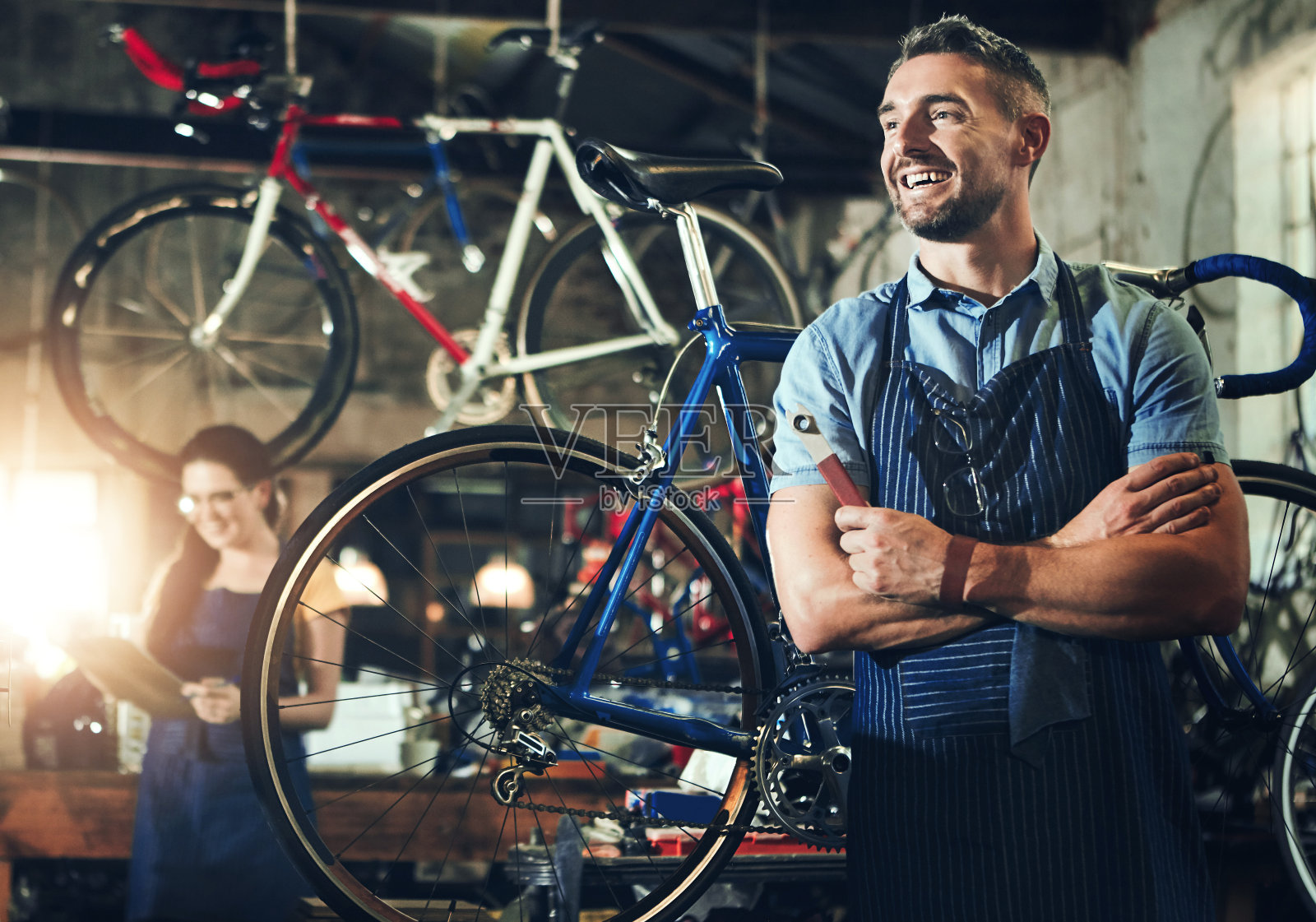 男人，微笑着双手交叉在自行车修理店或维修厂工作。自行车，机械师和专业勤杂工的服务，为创业思路，小企业和车间修理照片摄影图片