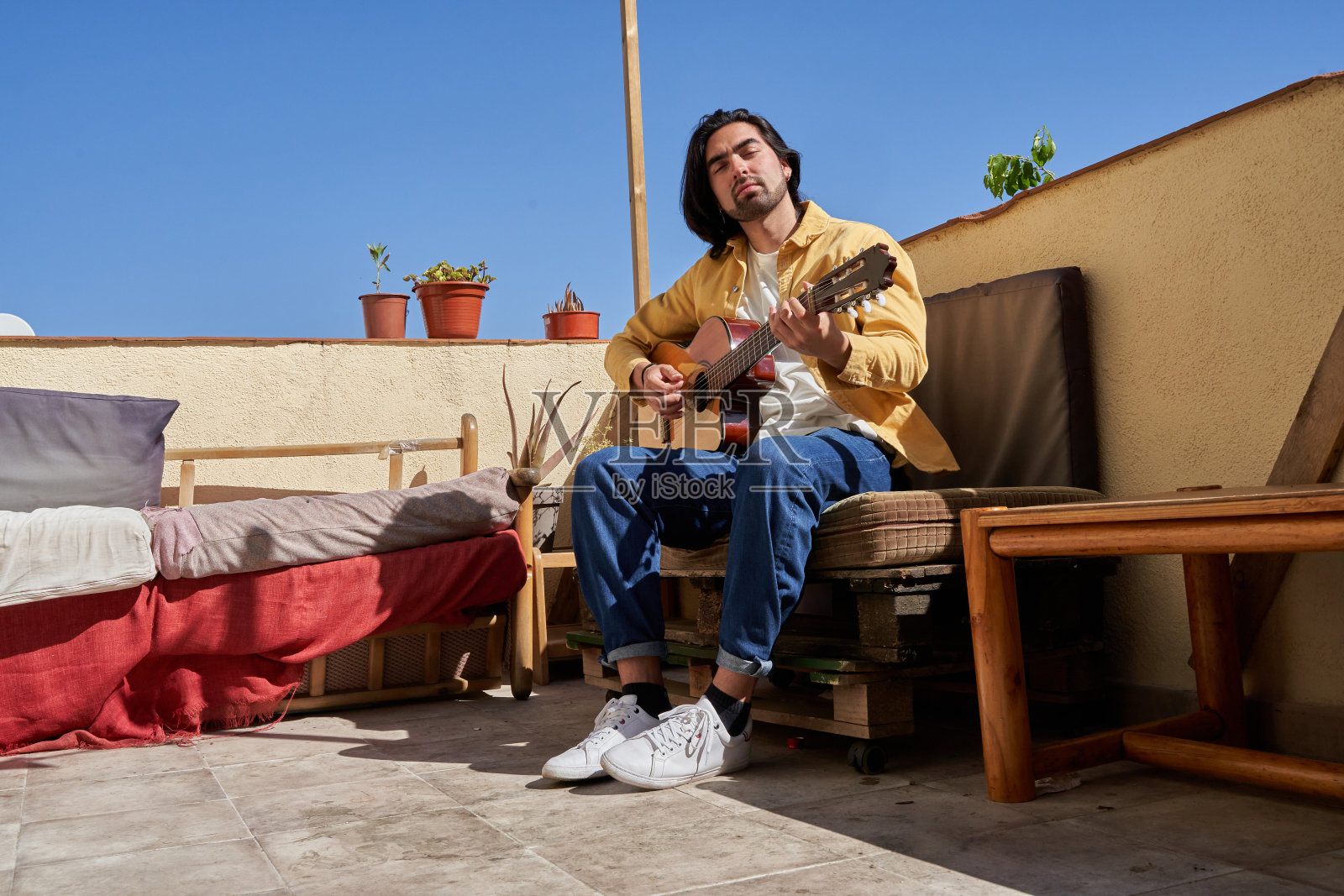 一个穿黄色衬衫的男人正在阳台上弹吉他。这个场景是轻松而宁静的，男人在一个舒适的环境中享受着他的音乐照片摄影图片