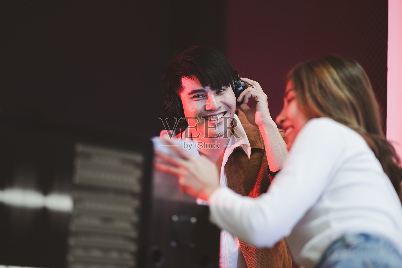 身穿白衬衫的亚洲制作人站在调音台前。快乐的女性音乐作曲家艺术家与一个男人歌手的背景照片摄影图片