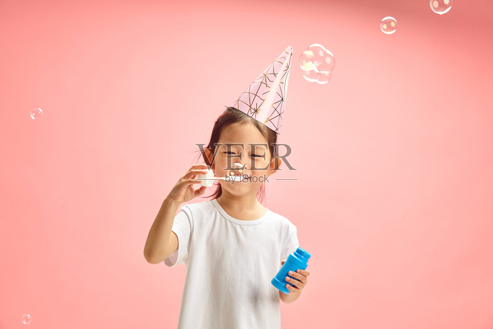可爱的小女孩在自己的生日期间吹着肥皂泡，站在粉红色的孤岛上照片摄影图片