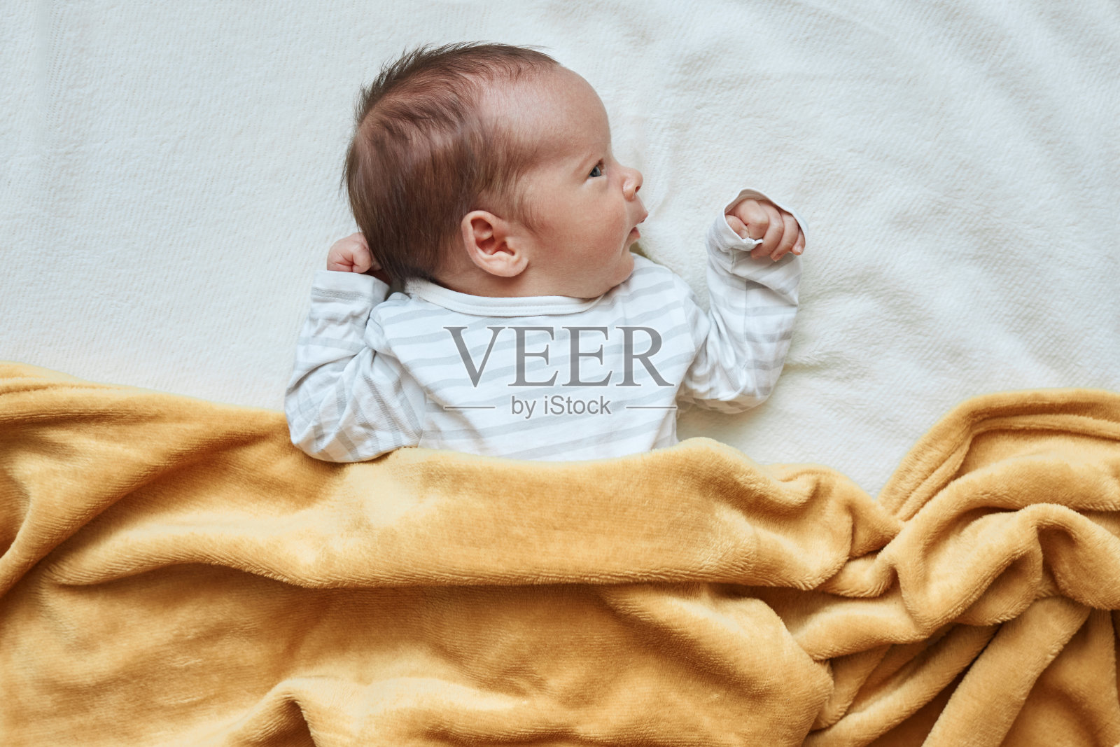 男婴躺在床上，穿着条纹童装，健康的新生儿躺在柔软的黄色格纹下照片摄影图片