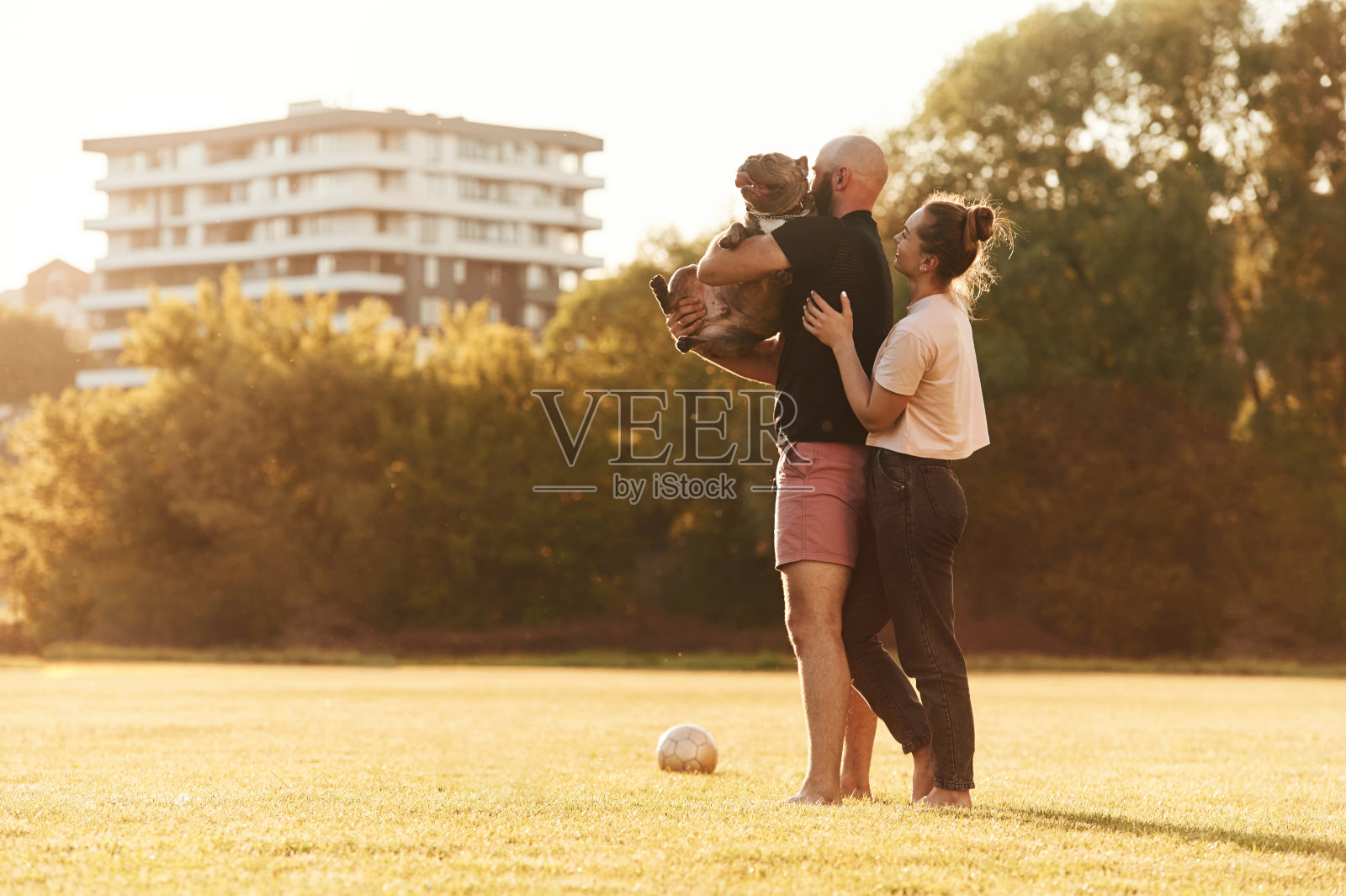 侧视图，站着抱着动物。一男一女带着狗在操场上照片摄影图片
