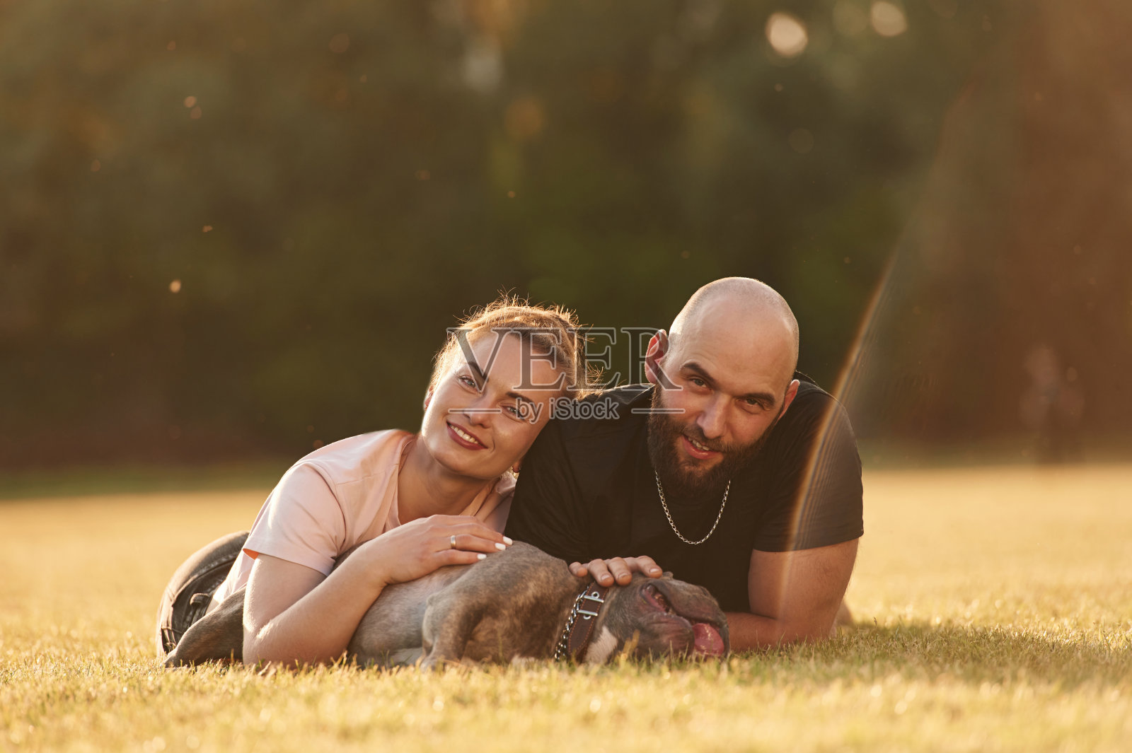 冷静，躺在地上。一男一女带着狗在操场上照片摄影图片