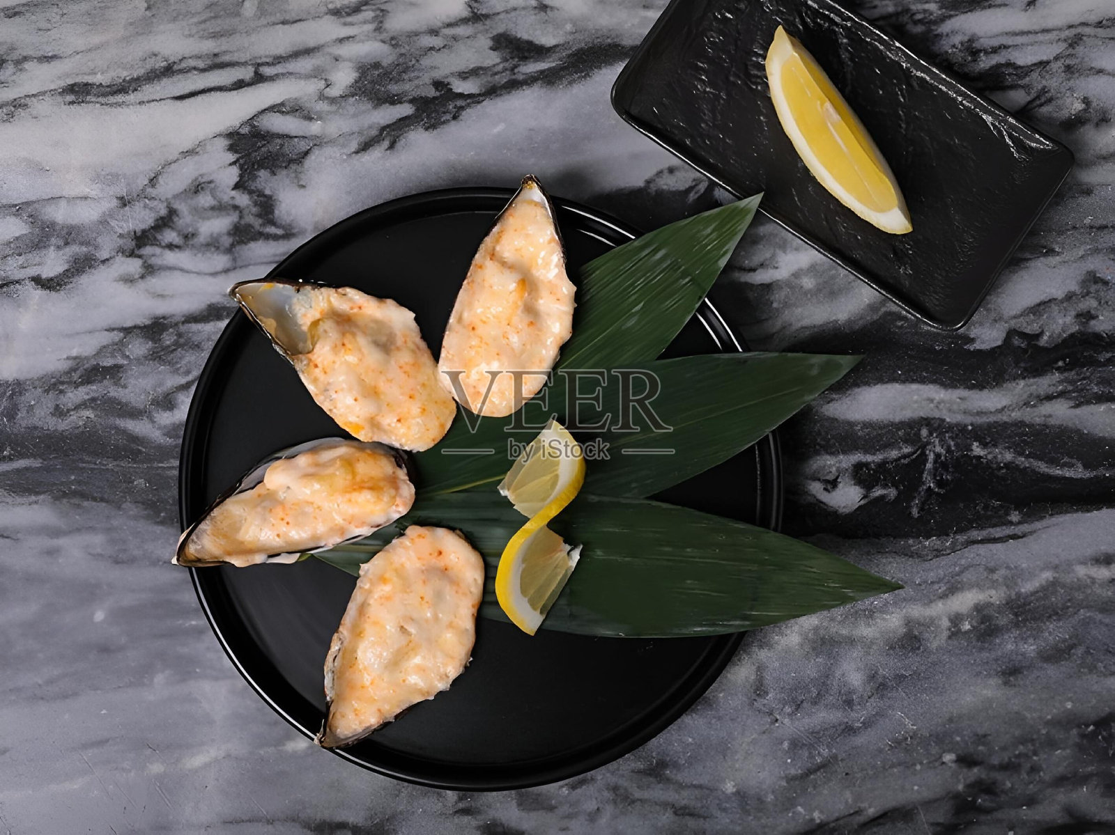 黑盘子上的烤贻贝配上奶油酱，配上柠檬角照片摄影图片