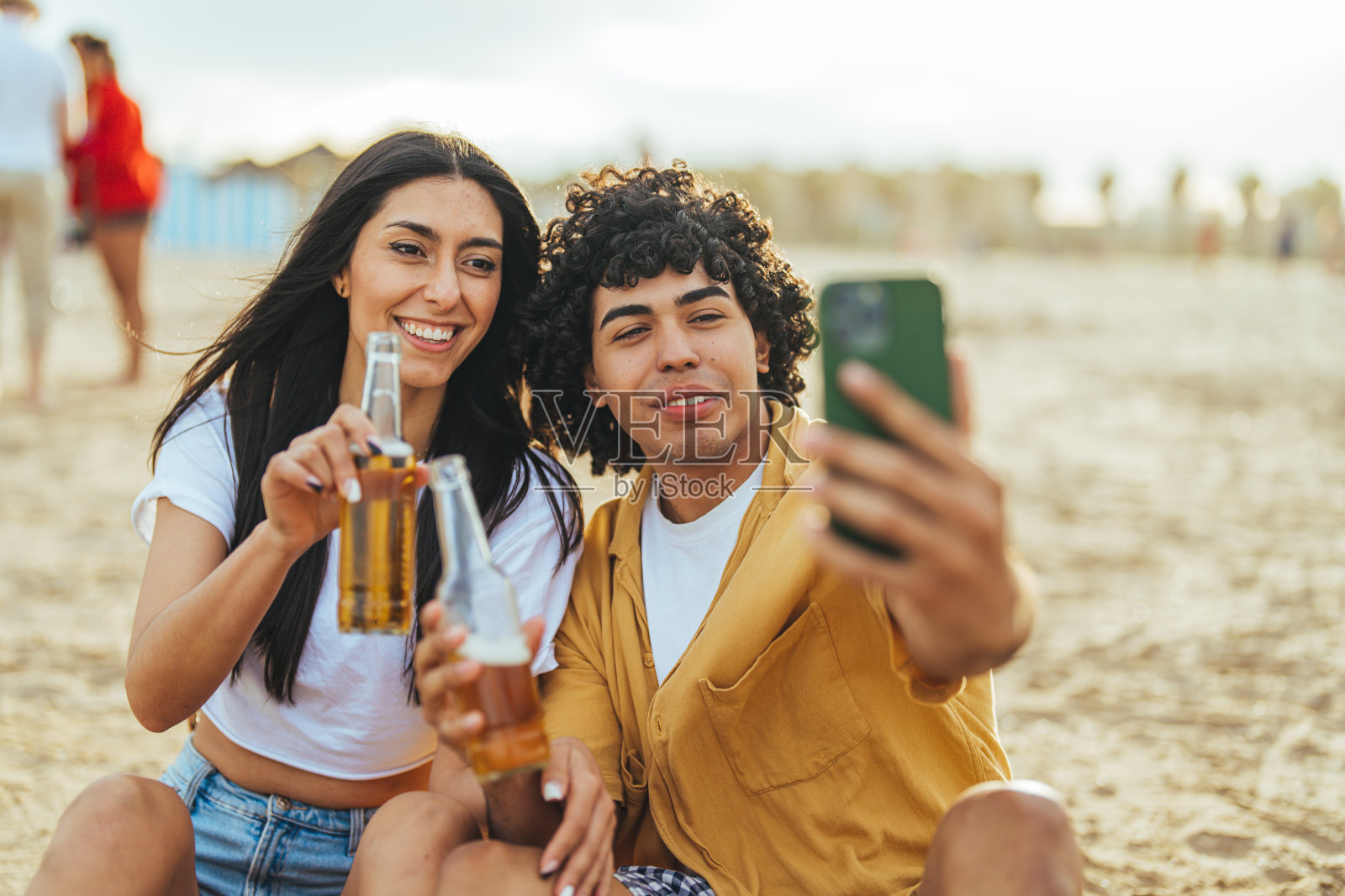 年轻的西班牙夫妇喝着啤酒在海滩自拍照片摄影图片