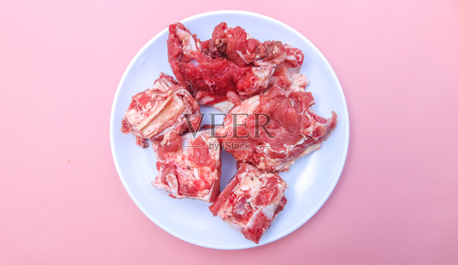 切片的骨头和新鲜的生牛肉放在白色的盘子里，在粉红色的背景上分开。新鲜排骨照片摄影图片