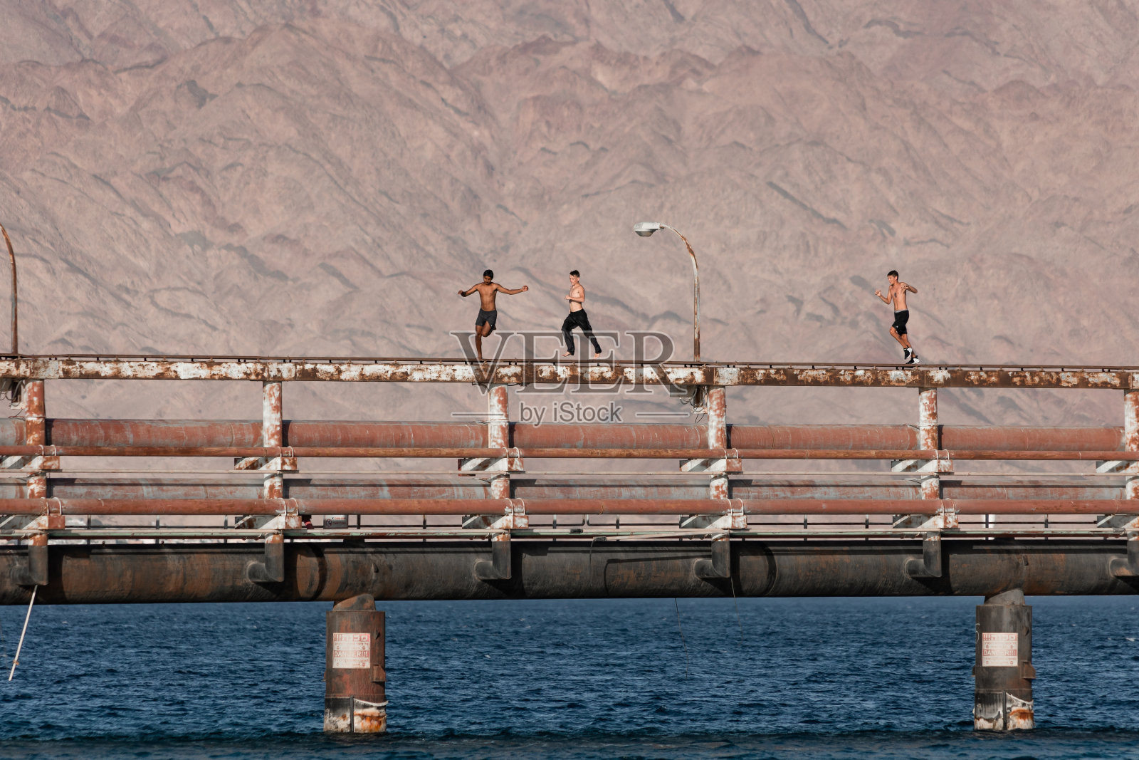 红海埃拉特卡察海滩的旧油港，带柱子的码头，青少年从码头跳水照片摄影图片
