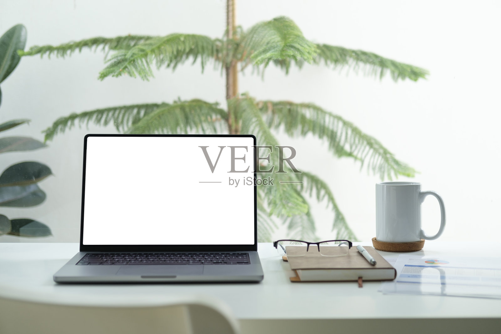 靠窗的白色办公桌上放着黑屏笔记本电脑、记事本和一杯咖啡。照片摄影图片