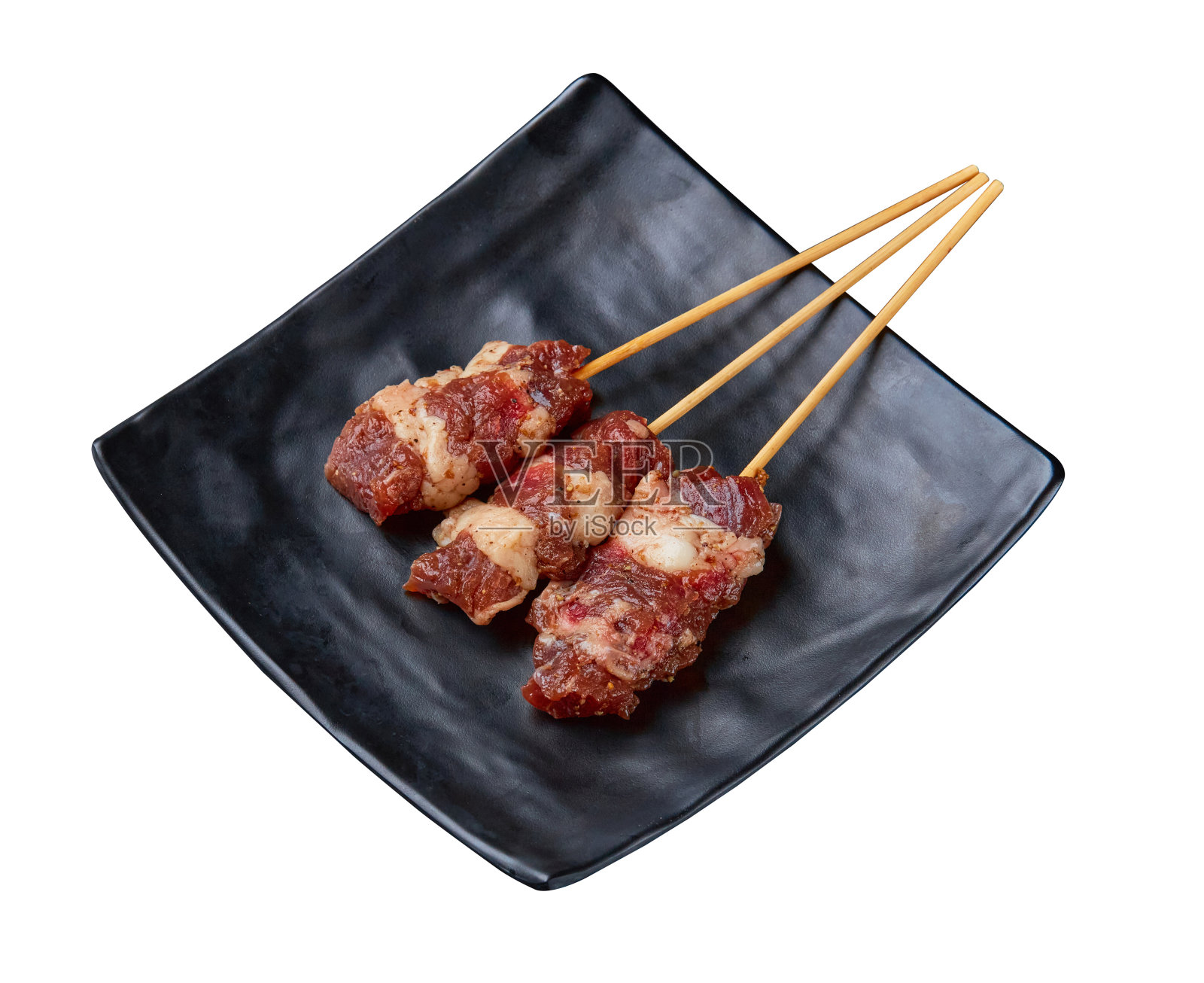 干熟牛肉，经过腌制和串好准备烧烤，装在白色背景上的黑色盘子里。照片摄影图片