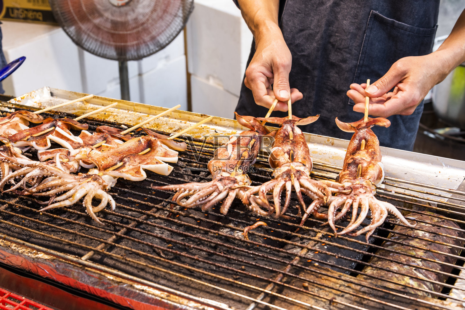 在夜市的烤架上堆叠许多烤鱿鱼串。照片摄影图片