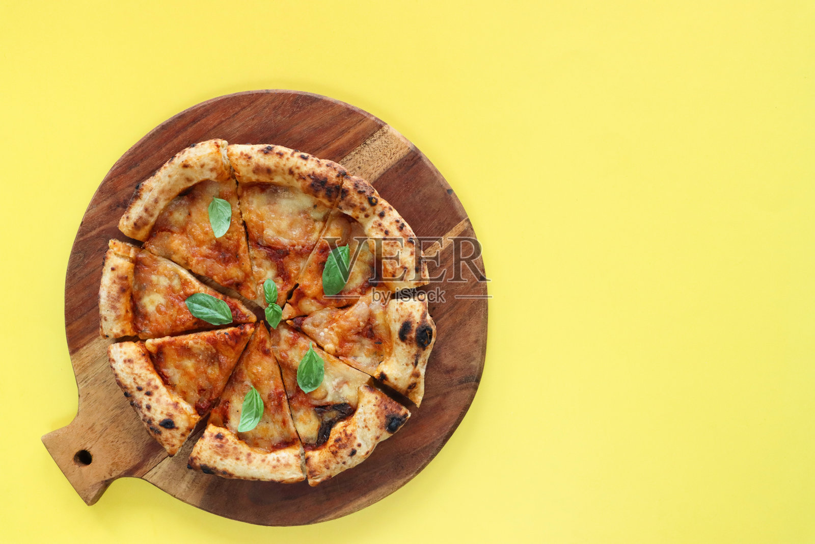 切片的玛格丽塔披萨放在圆形的木制砧板上，融化的金色水牛马苏里拉奶酪，丰富的番茄马里纳拉酱和新鲜的罗勒叶浇头，黄色背景，高架视图，复制空间照片摄影图片