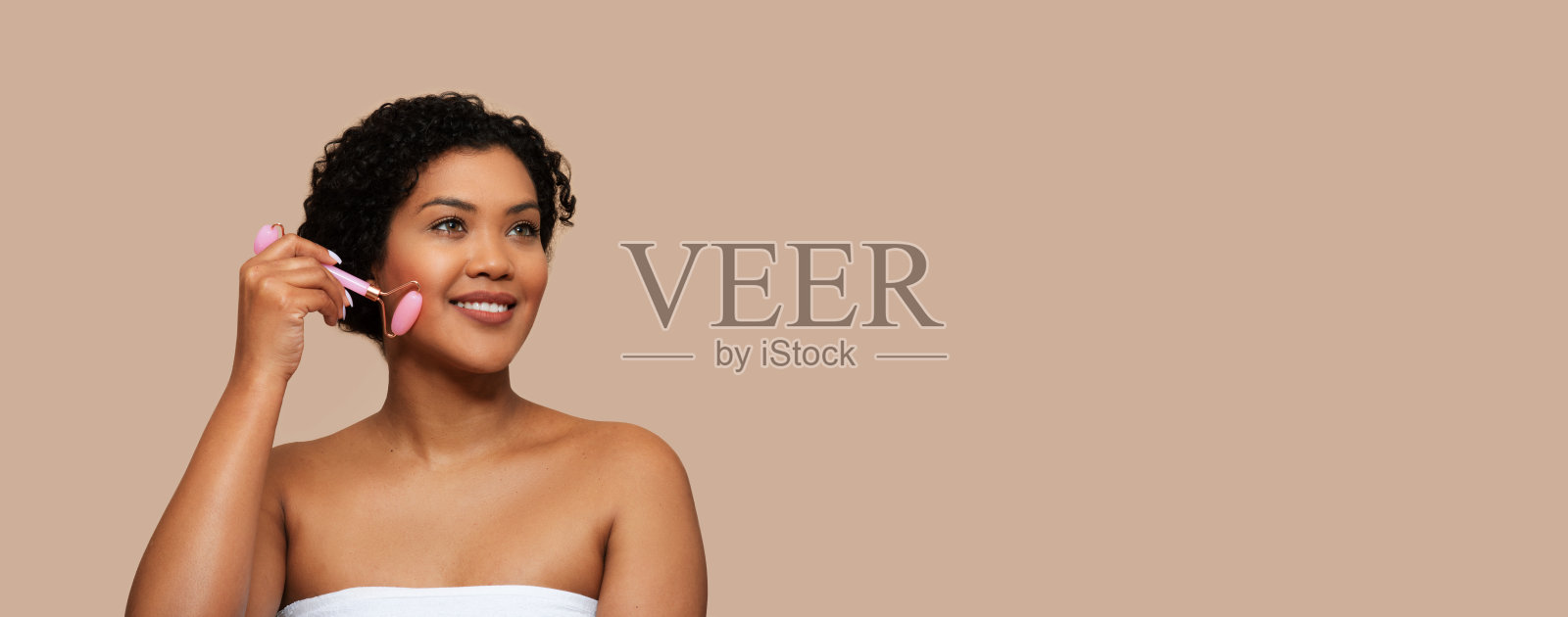 美丽的年轻巴西女士裹在毛巾使用面部滚筒照片摄影图片