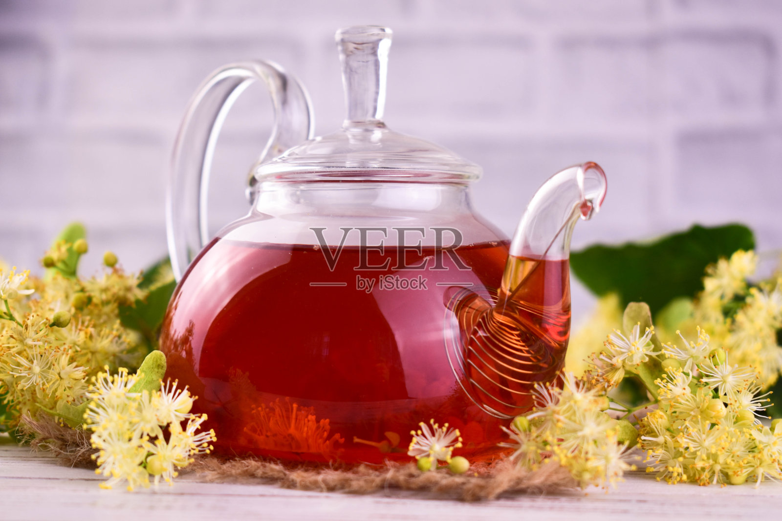 茶从菩提花在一个透明的茶壶对新鲜的菩提花的背景。照片摄影图片