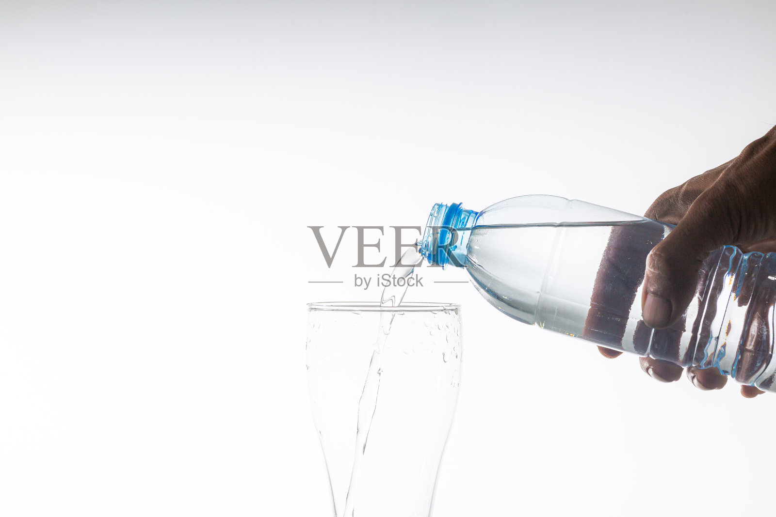 人的手往杯子里倒饮用水，白色背景，孤立;人的手拿着塑料水瓶，往杯子里倒水，白色背景照片摄影图片