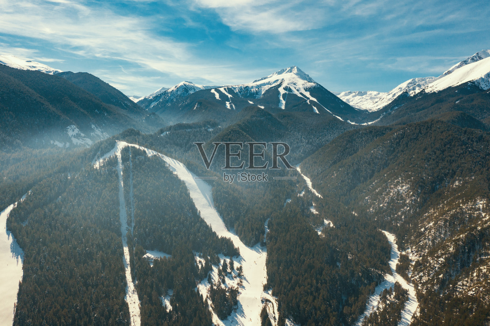 鸟瞰明亮的全景山脉与雪顶在冬天的蓝天。阳光下的高山。青山和茂密的森林。松林。放松。无人机。大自然。旅游的概念照片摄影图片