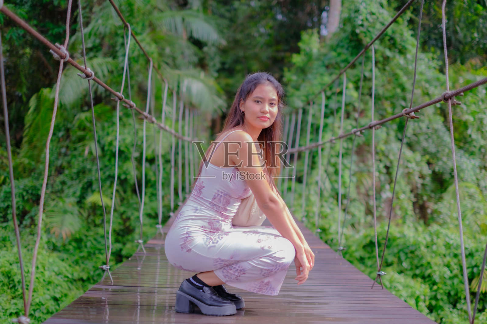 一位年轻的亚洲女子走在一座以森林为背景的桥上。照片摄影图片