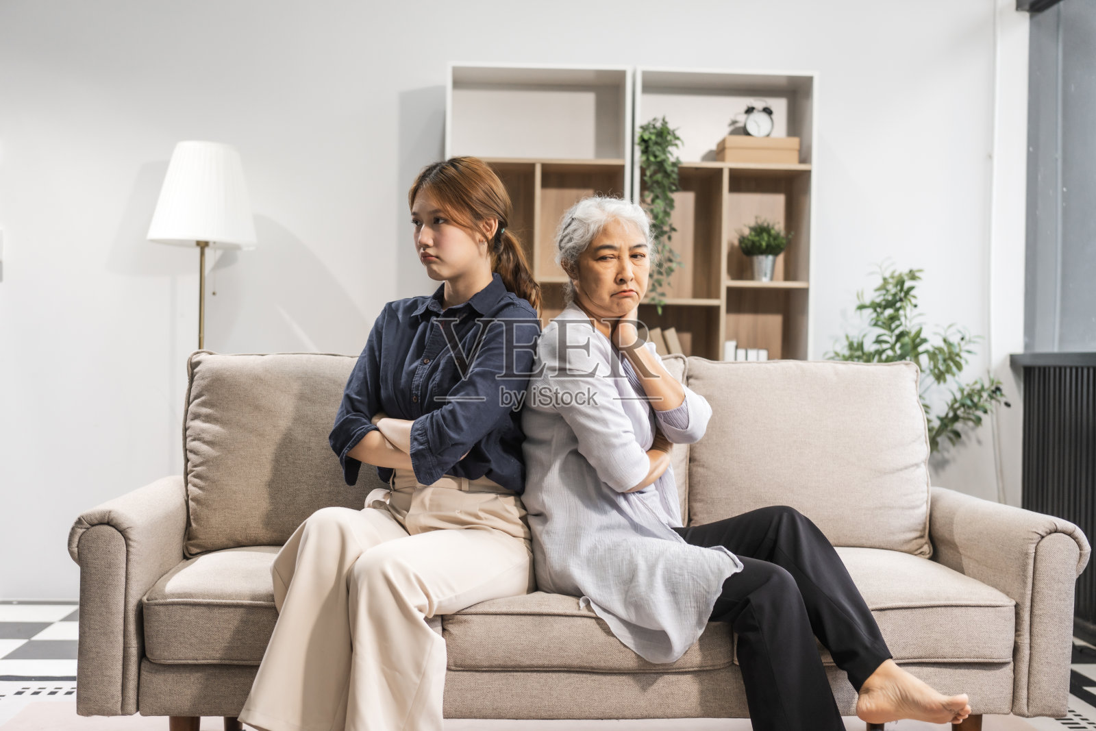 一位成熟的母亲和她年幼的女儿，都是亚洲人，坐在沙发上吵架。他们的争论升级为冲突，因为误解而产生冲突和摩擦。照片摄影图片