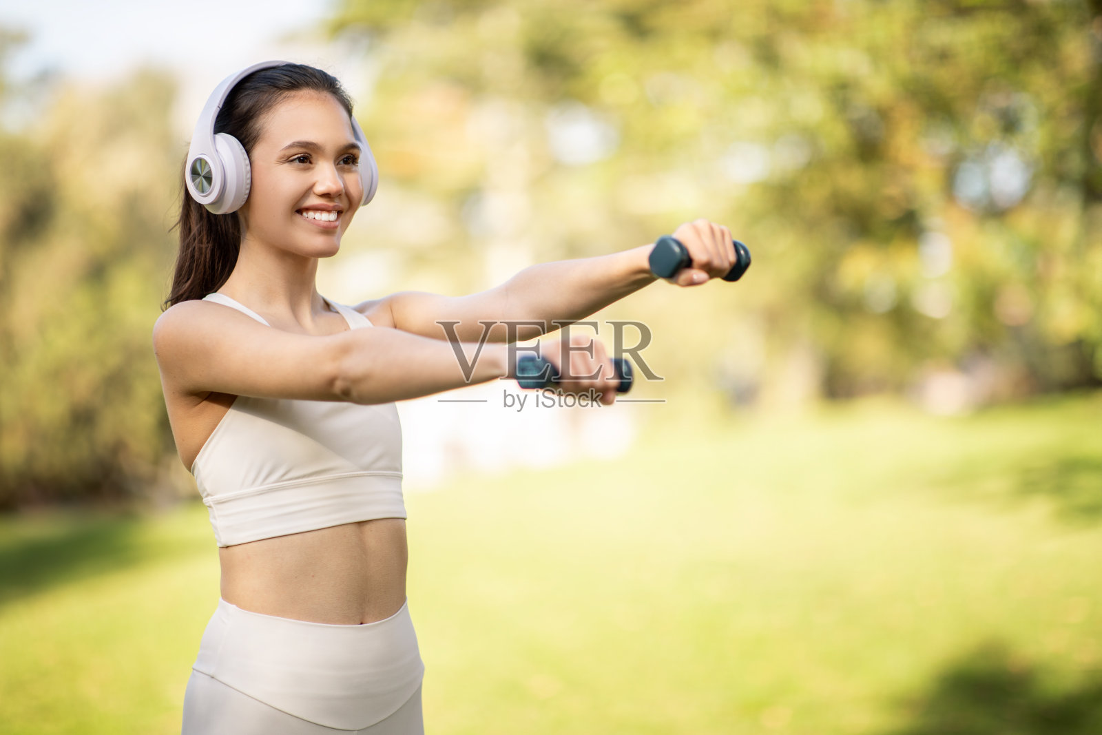 身穿米色运动服的容光焕发的年轻女子在户外使用手举重物照片摄影图片