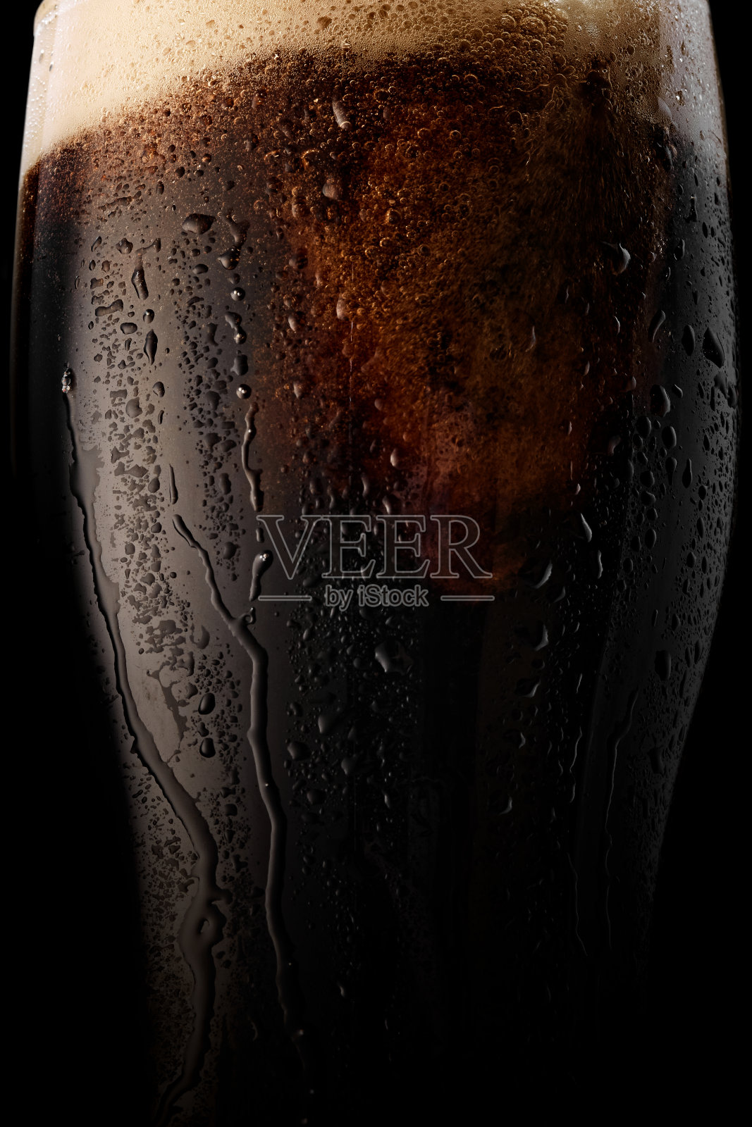 近距离拍摄的丰富的黑啤酒在玻璃，与凝露和奶油泡沫头在黑色的背景。照片摄影图片