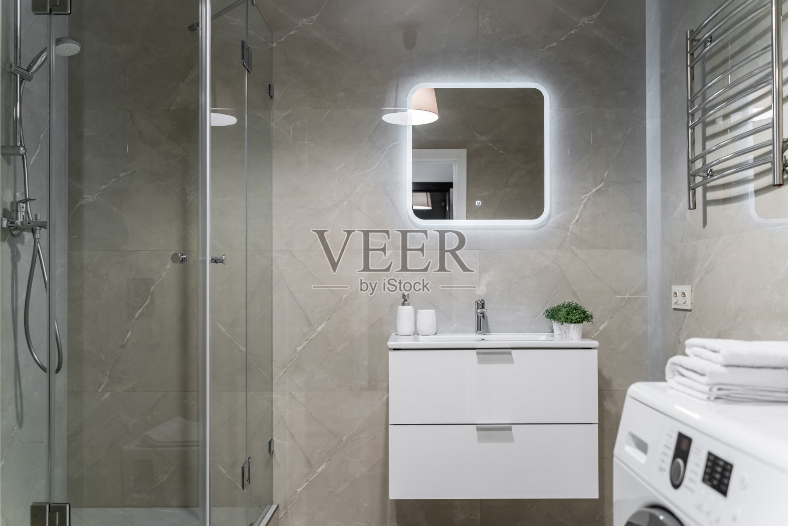 现代的浴室设计，浅色的瓷砖，白色的家具和白色的马桶。带滑动门的玻璃淋浴房照片摄影图片