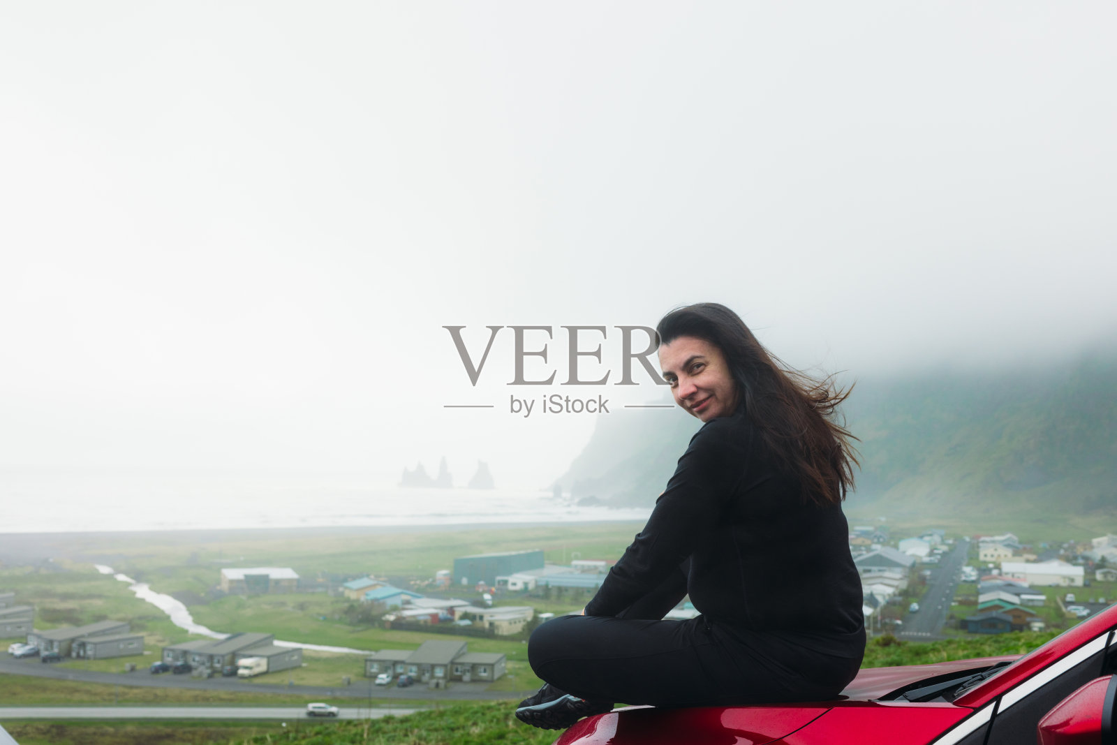 成熟的女性旅行者在红色轿车上凝视着雾中山间海滩的壮观景色照片摄影图片