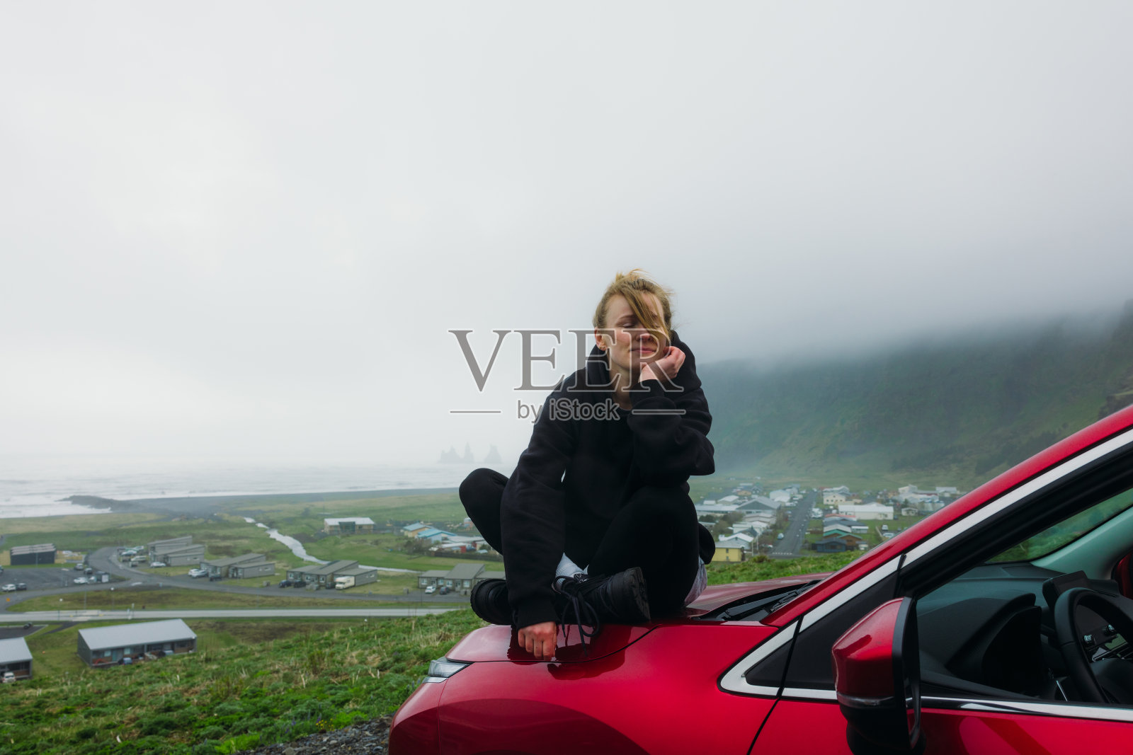女旅行者坐在红色的轿车上，在雾中欣赏山间海滩的壮观景色照片摄影图片