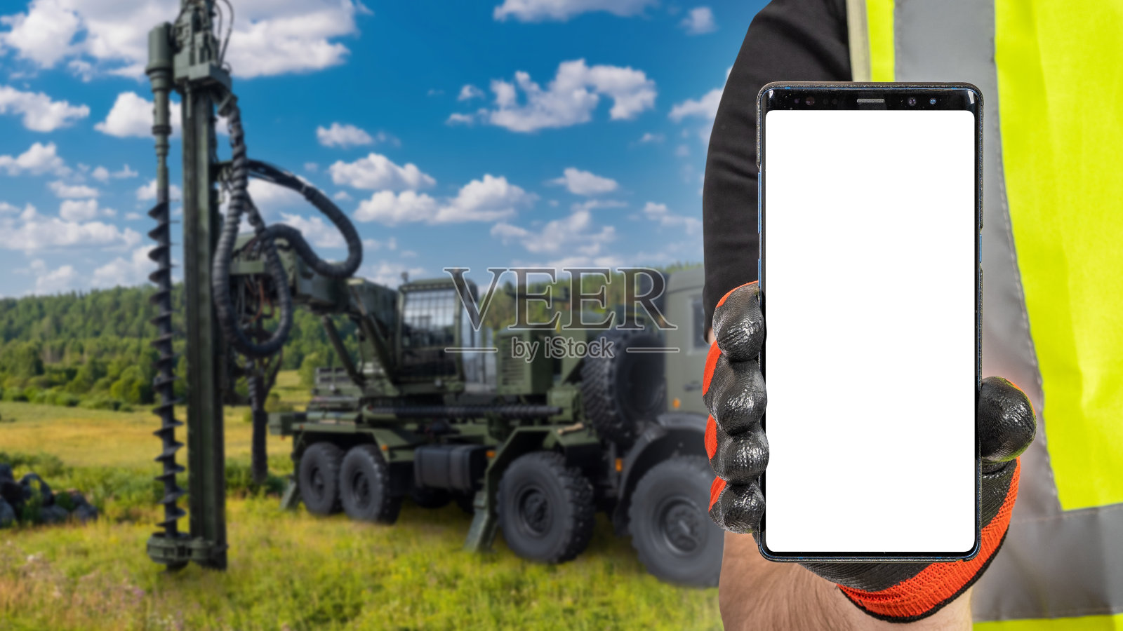 建设业务。建筑商手里拿着电话。用于地下钻井的机器。黑屏手机。钻井取水。施工期间开发水井。艺术的焦点照片摄影图片