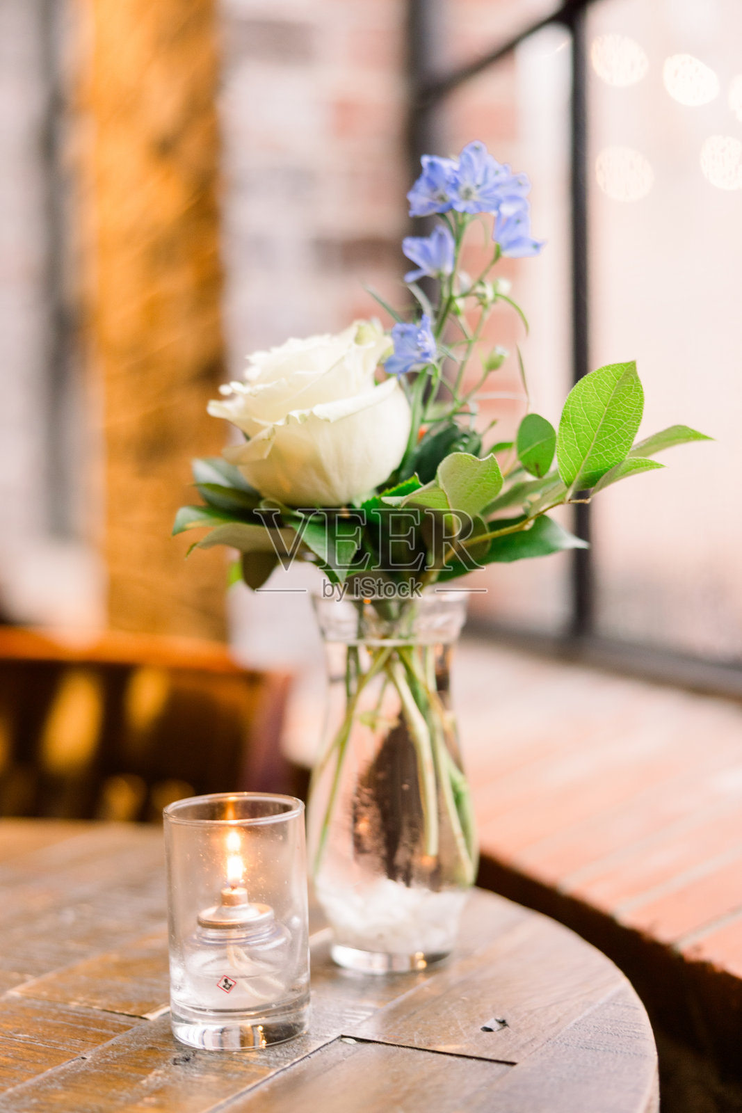 一瓶水里插着一朵简单的玫瑰和绿色植物，桌上放着一支蜡烛照片摄影图片