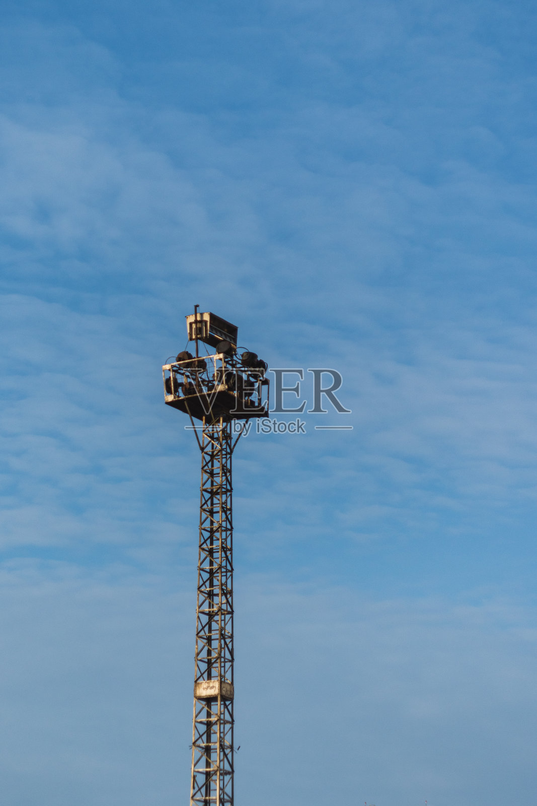 一座孤零零的灯塔矗立在蔚蓝的天空下。塔的顶部安装了一个带有照明设备的平台，通常用于照亮大型公共场所、建筑工地或户外活动。照片摄影图片