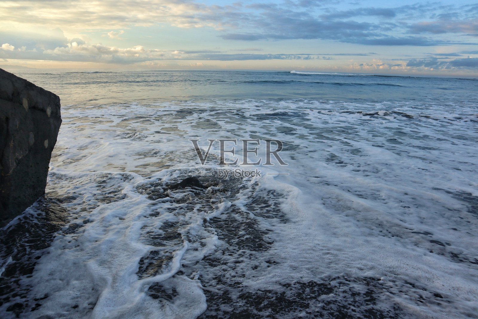 海滩是黑色的沙子和海浪，覆盖着泡沫的海浪。美丽的日出照片摄影图片