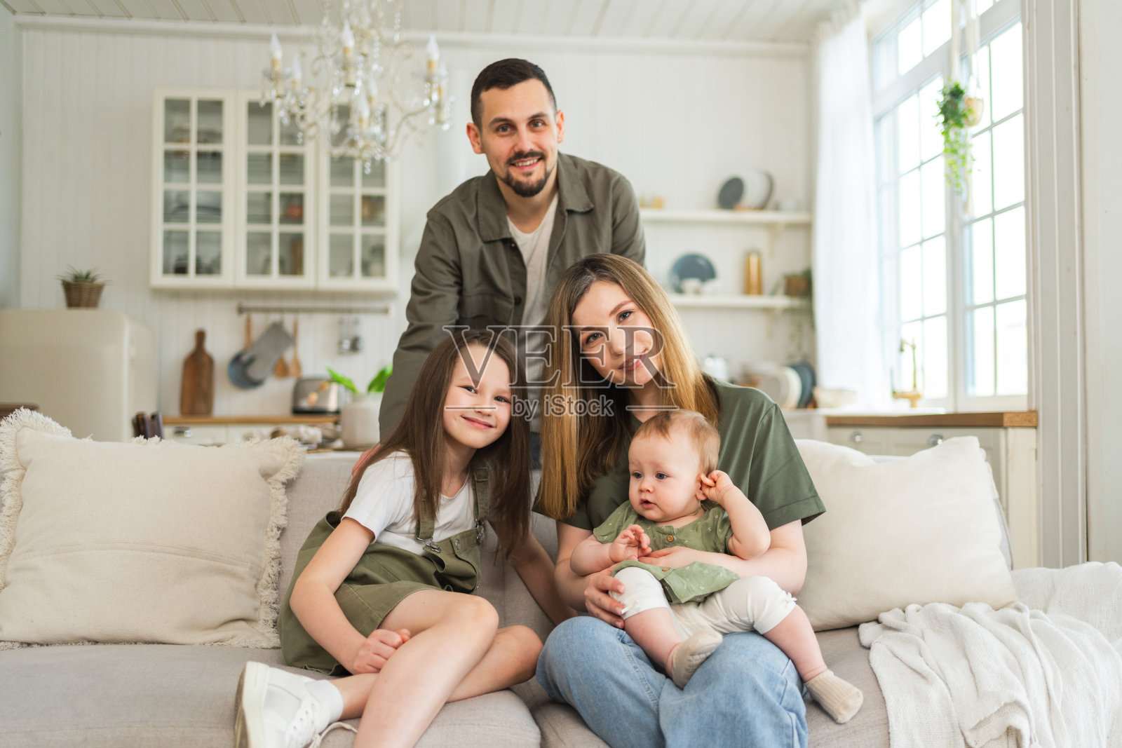 家庭美满。妈妈、爸爸、两个孩子、女儿在室内的沙发上休息。妈妈，爸爸，父母，宝宝，女孩，孩子，放松，一起玩，一起开心。一家人笑着享受温柔的时刻。照片摄影图片